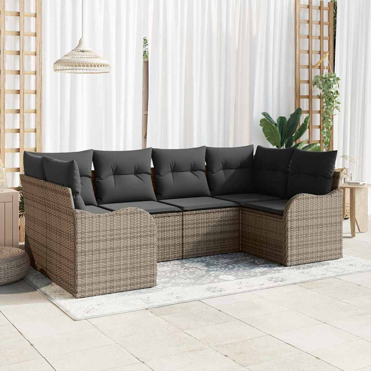 Ein Ecksofa aus Korbgeflecht mit grauen Kissen steht auf einem Teppich. Weiße Vorhänge und eine Hängelampe sind im Hintergrund.