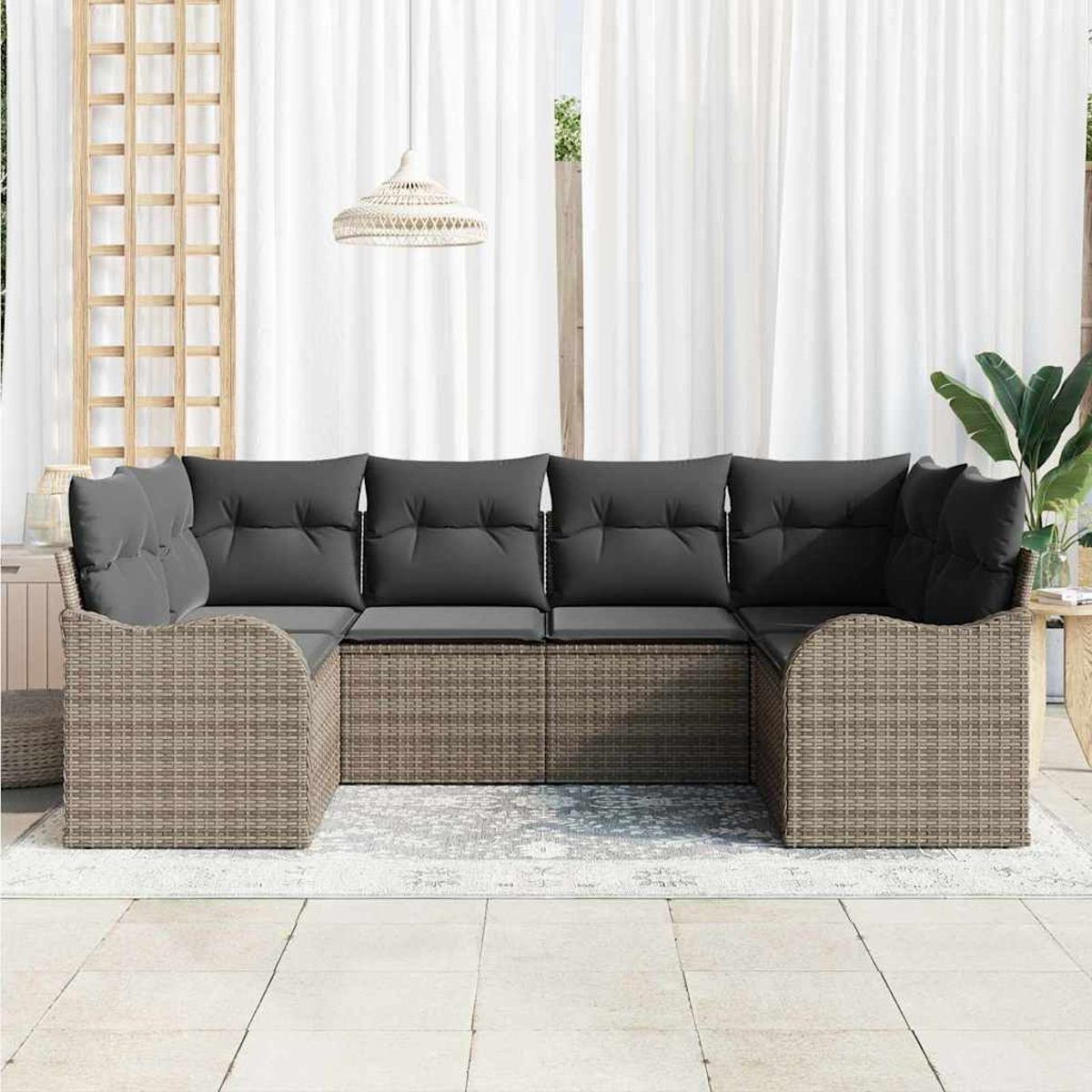 Ein Rattansofa mit grauen Kissen steht auf einem Teppich. Weiße Vorhänge dahinter, mit einer hängenden Web-Leuchte.