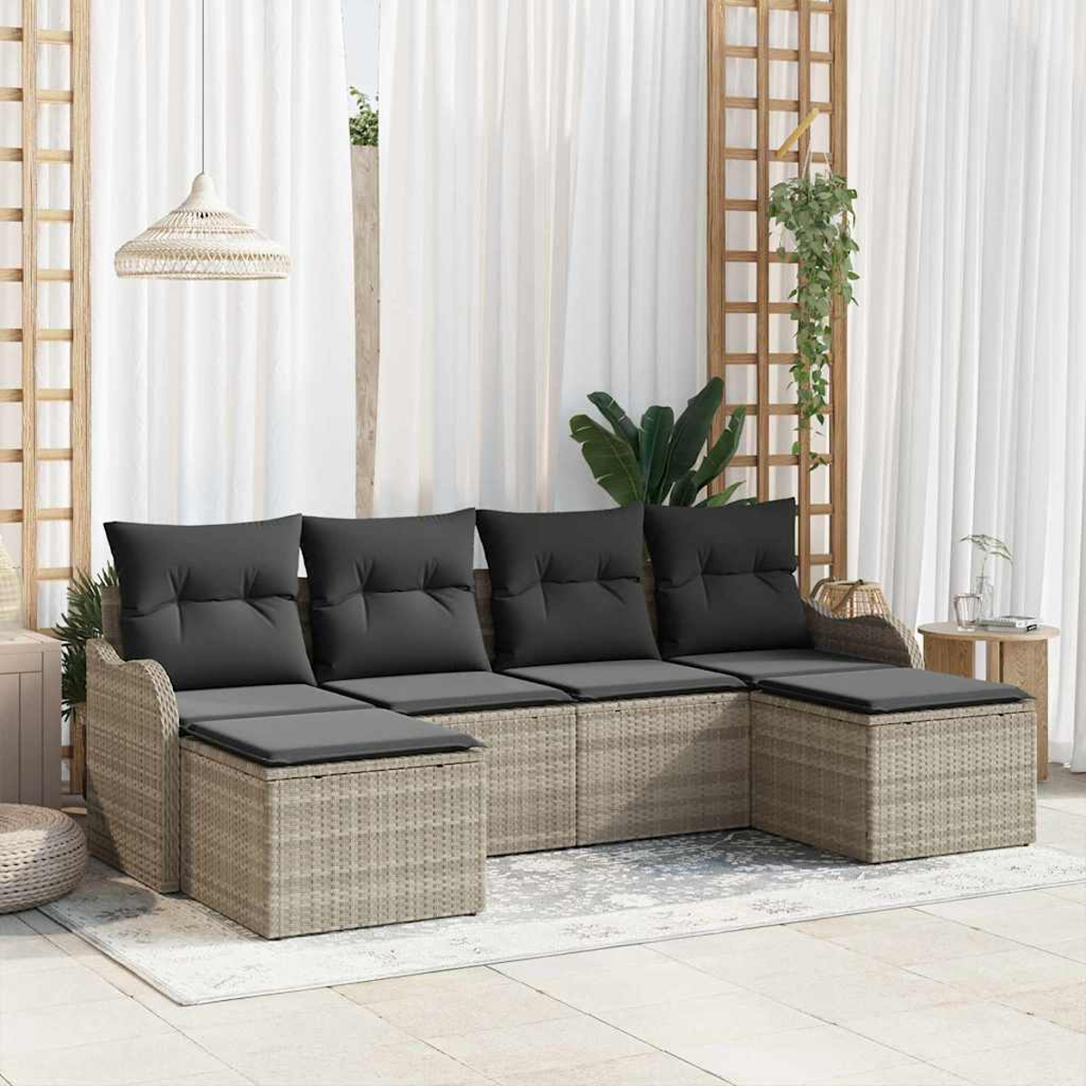 Ein Rattansofa mit schwarzen Kissen steht auf einer Terrasse. Weiße Vorhänge und ein Holzgitter sind im Hintergrund.