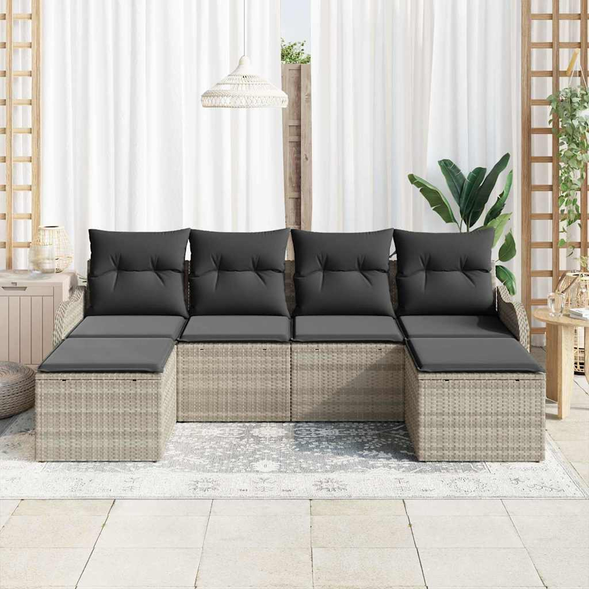 Ein graues Outdoor-Ecksofa aus Korbgeflecht mit dunkelgrauen Kissen steht auf einer Terrasse. Weiße Vorhänge und Pflanzen sind im Hintergrund.
