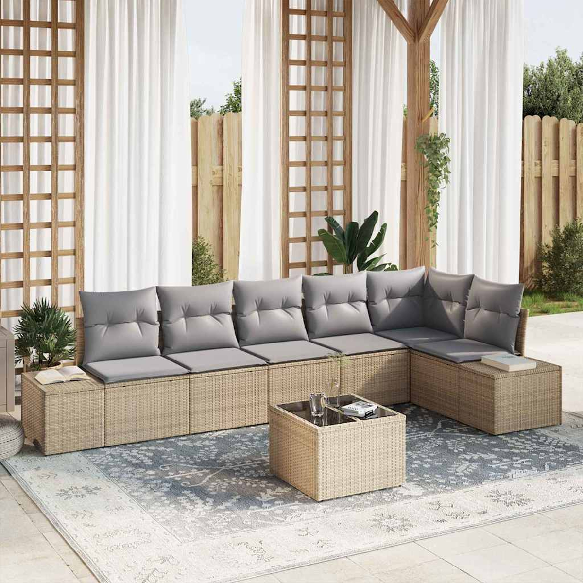 Ein Outdoor-Terrassen-Set mit grauen Kissen und einem kleinen Tisch steht auf einem gemusterten Teppich. Weiße Vorhänge und eine Holzstruktur spenden Schatten.