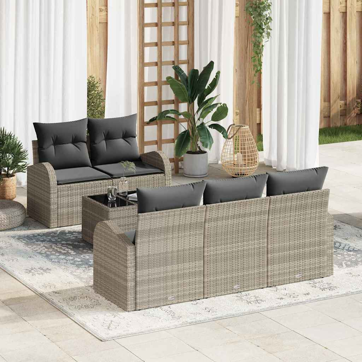 Terrassenset mit grauen Kissen. Enthält eine Couch, ein Sofa und einen Couchtisch auf einem gemusterten Teppich. Pflanzen und Vorhänge im Hintergrund.