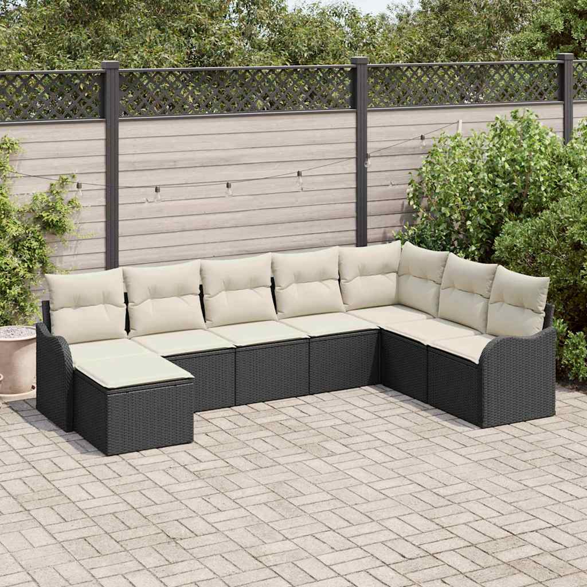 Un sofá seccional para exteriores gris oscuro con cojines beige. Está en un patio. Una valla de madera y vegetación están en el fondo.