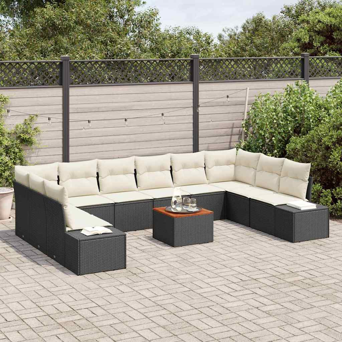 Ein Outdoor-Terrassenset mit schwarzen Korbmöbeln und beigen Kissen. In der Mitte steht ein kleiner Tisch mit Getränken. Im Hintergrund ist ein Holzzaun.