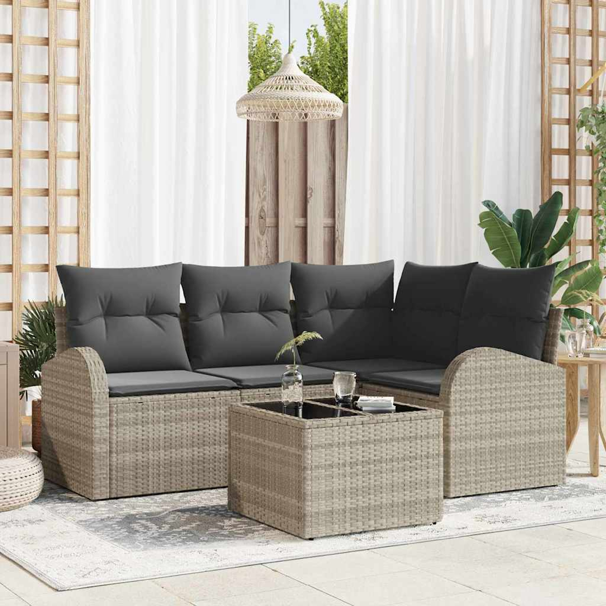 Outdoor-Korbsessel mit dunkelgrauen Kissen und einem passenden Couchtisch. Weiße Vorhänge und Pflanzen sind im Hintergrund.