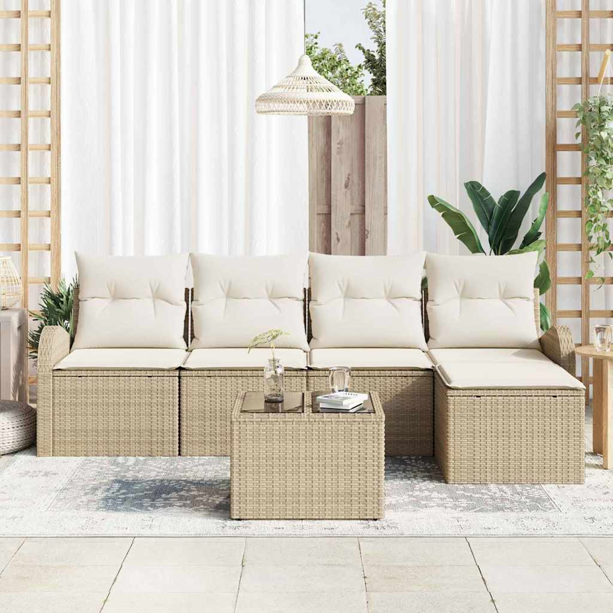 Geflochtenes Outdoor-Ecksofa mit cremefarbenen Kissen und einem quadratischen Couchtisch. Weiße Vorhänge und eine Hängelampe vervollständigen die Szene.