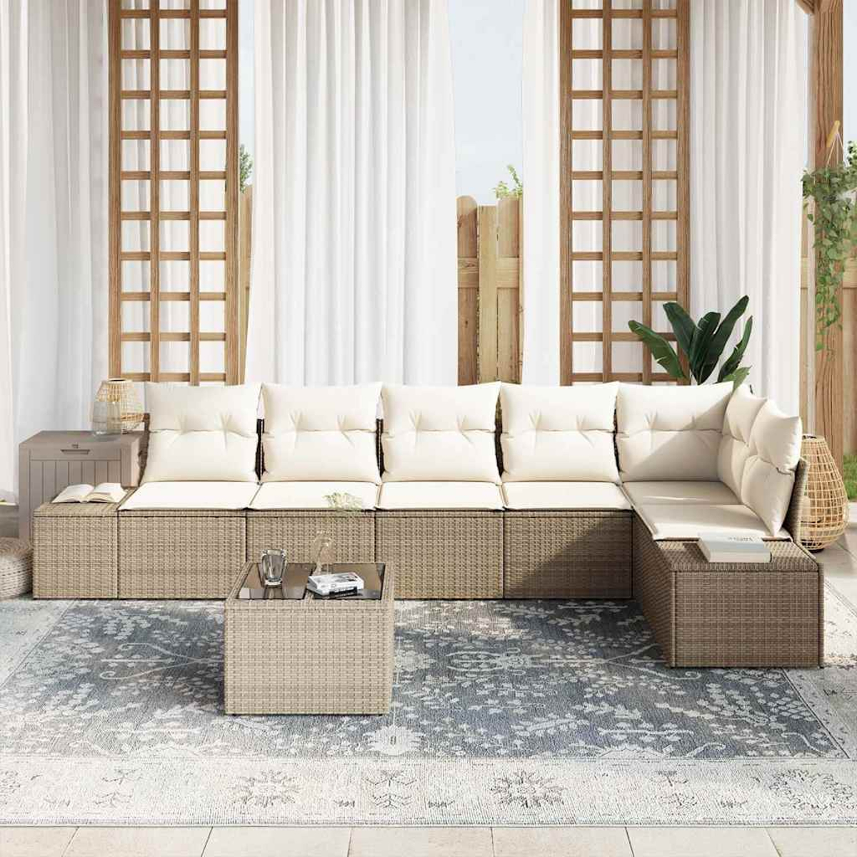 Outdoor-Sitzbereich mit beigen Korbmöbeln, weißen Kissen, einem Couchtisch und einem gemusterten Teppich. Weiße Vorhänge und Holzgitter sichtbar.