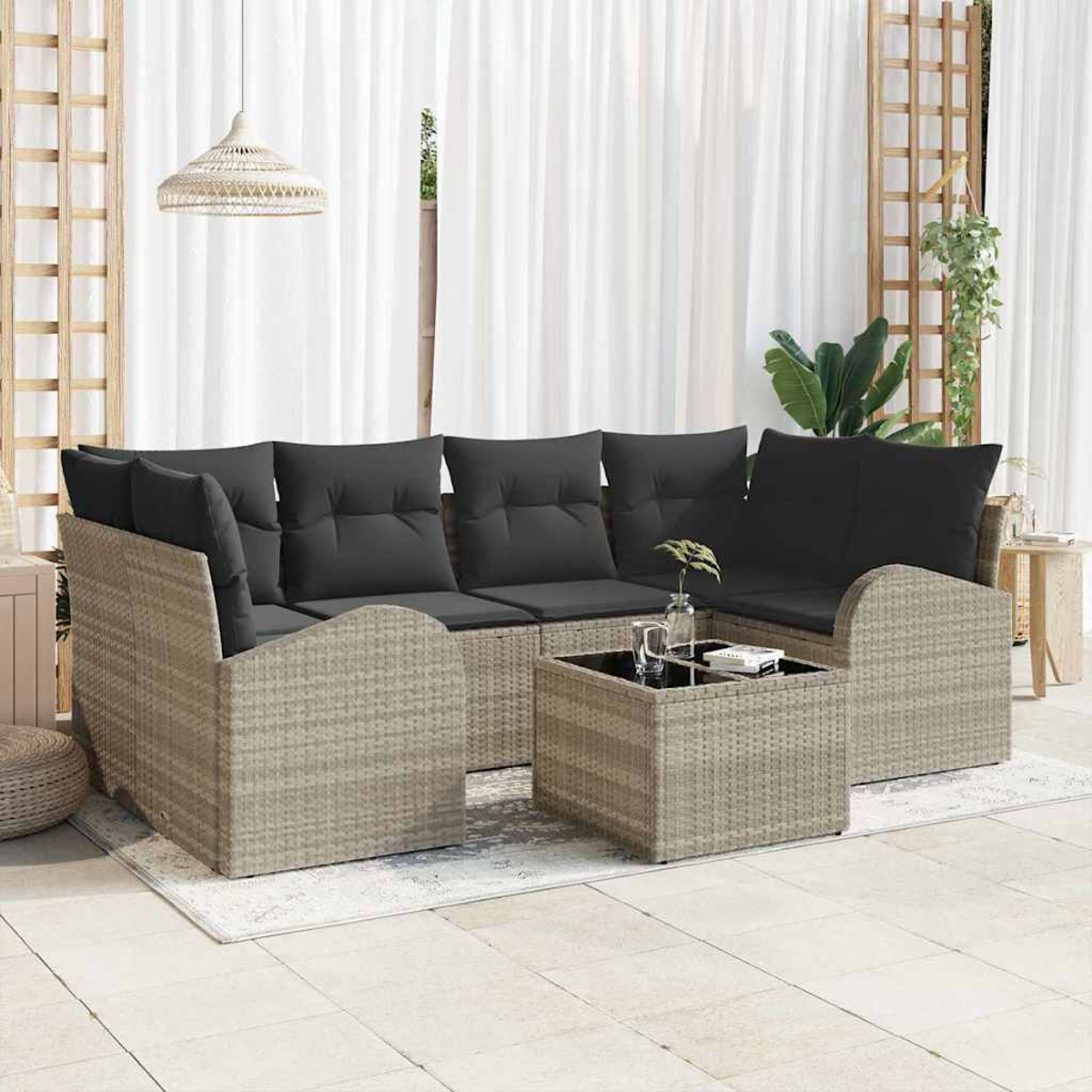 Juego de sofás de mimbre para exteriores con cojines grises, mesa con tapa de cristal y cortinas blancas.