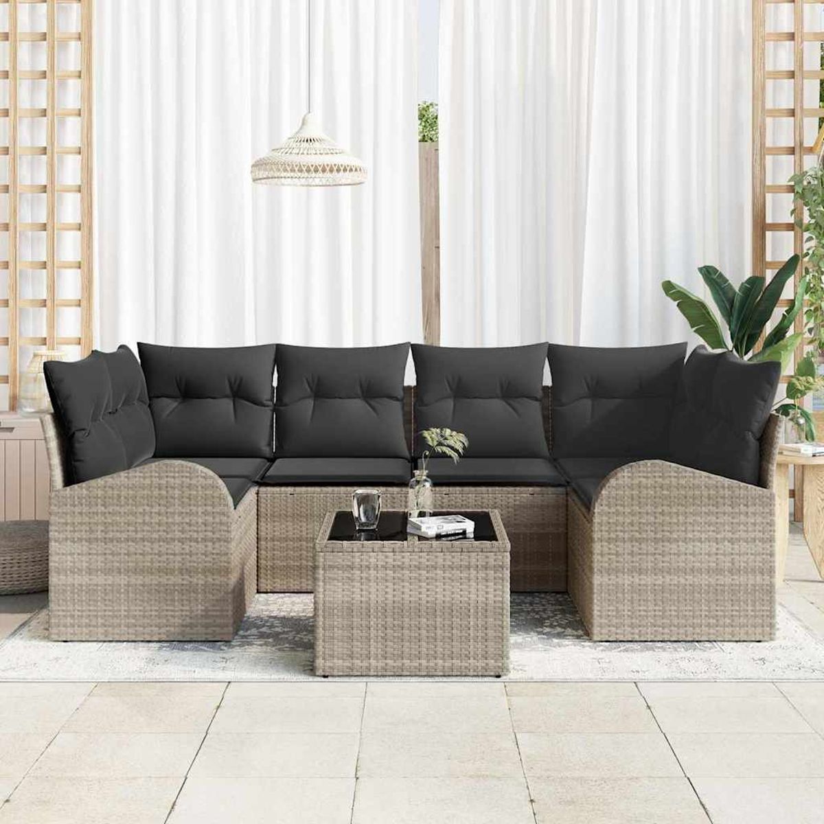 Seccional de mimbre para exteriores con cojines negros. Mesa de centro cuadrada con tapa de cristal. Cortinas blancas al fondo.