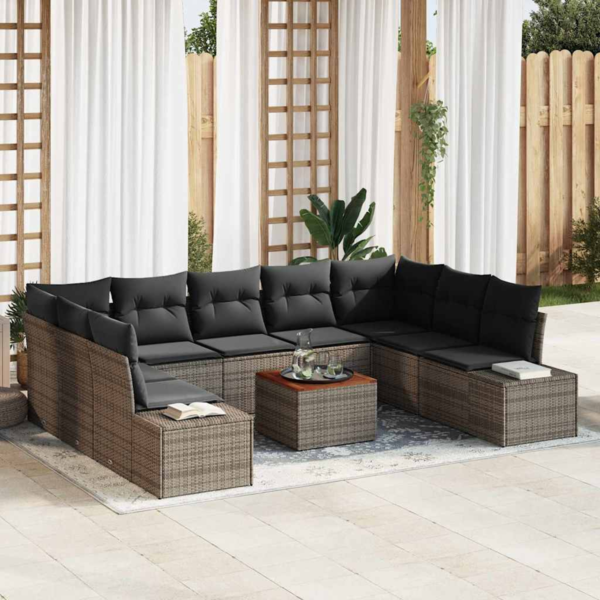 Garten-Ecksofa mit grauen Kissen, Couchtisch und transparenten weißen Vorhängen im Hintergrund. Holzzaun und Pflanzen sind ebenfalls sichtbar.