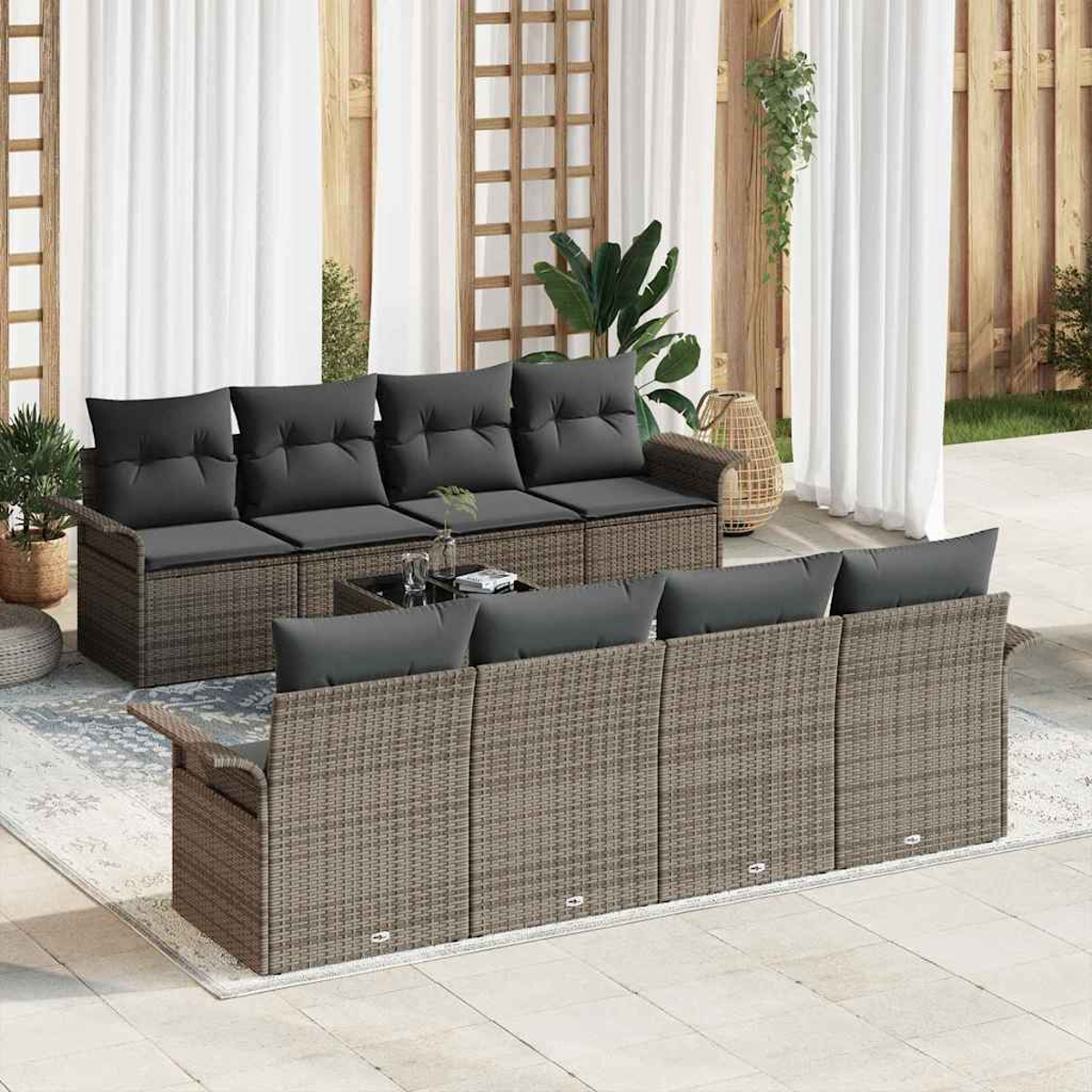Outdoor-Sitzarrangement mit Rattan-Sofas, grauen Kissen und einem Glastisch. Auf einer Terrasse mit weißen Vorhängen im Hintergrund.