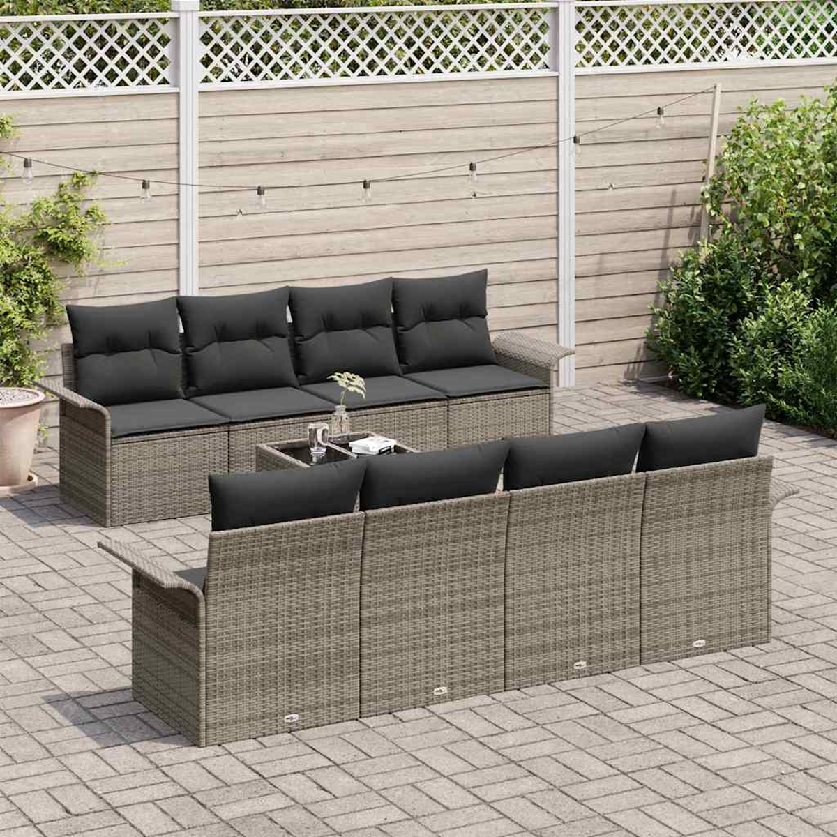 Garten-Rattan-Möbelset mit schwarzen Kissen auf einer Terrasse. Enthält ein Sofa, eine Couch und einen kleinen Tisch vor einem Holzzaun.