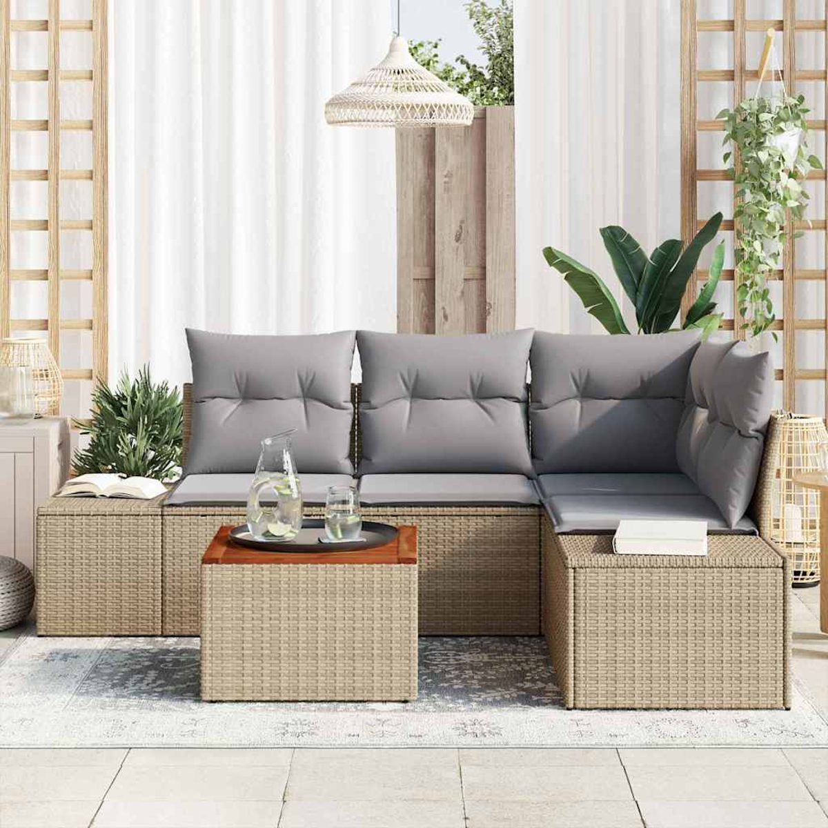 Outdoor-Sitzbereich mit gewebten Möbeln, grauen Kissen, einem Holztisch mit Getränken und Pflanzen. Weiße Vorhänge und eine Lampe sind im Hintergrund.