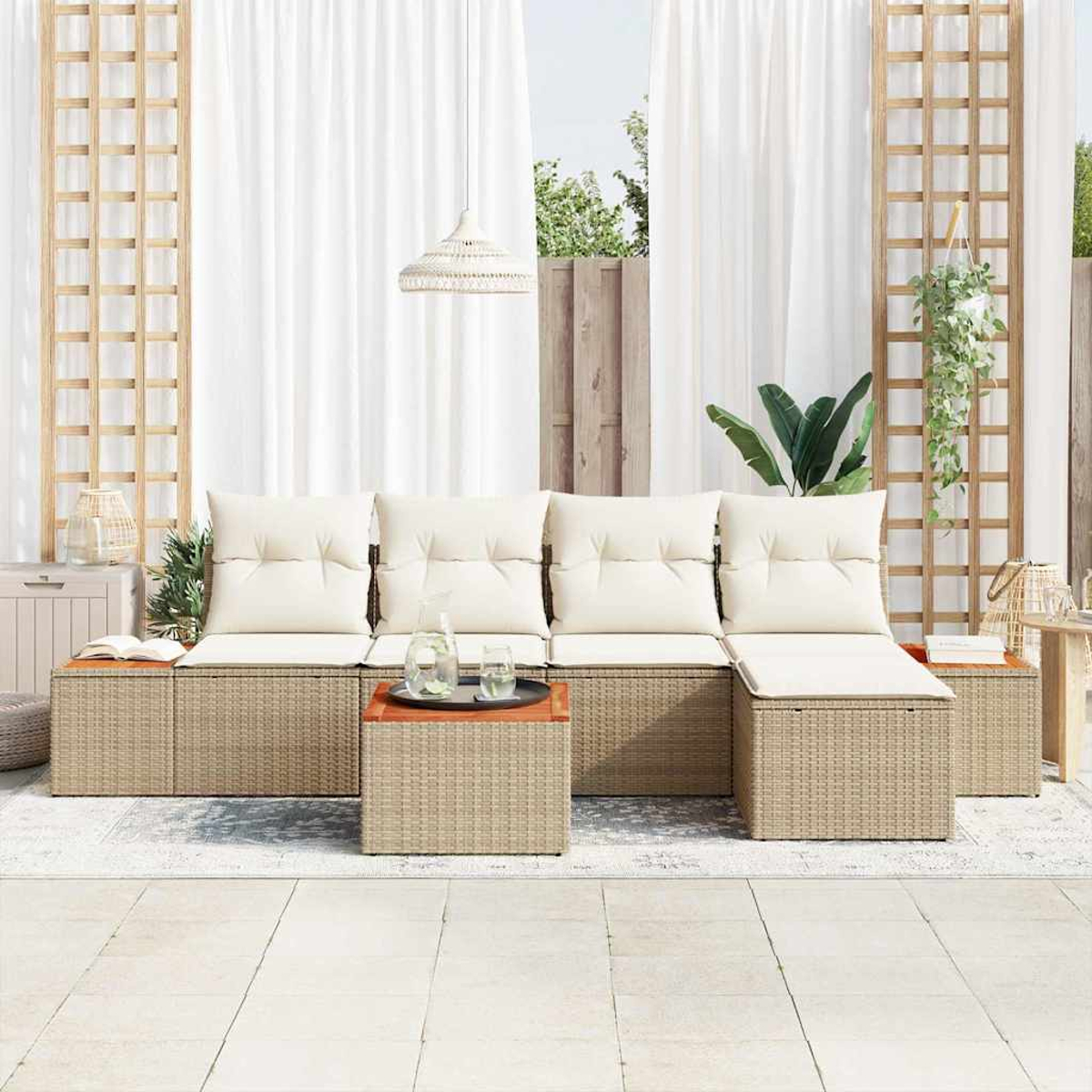 Gartenmöbel mit cremefarbenen Kissen. Ein gewebter Couchtisch mit Tablett und Gläsern, mit weißen Vorhängen im Hintergrund.