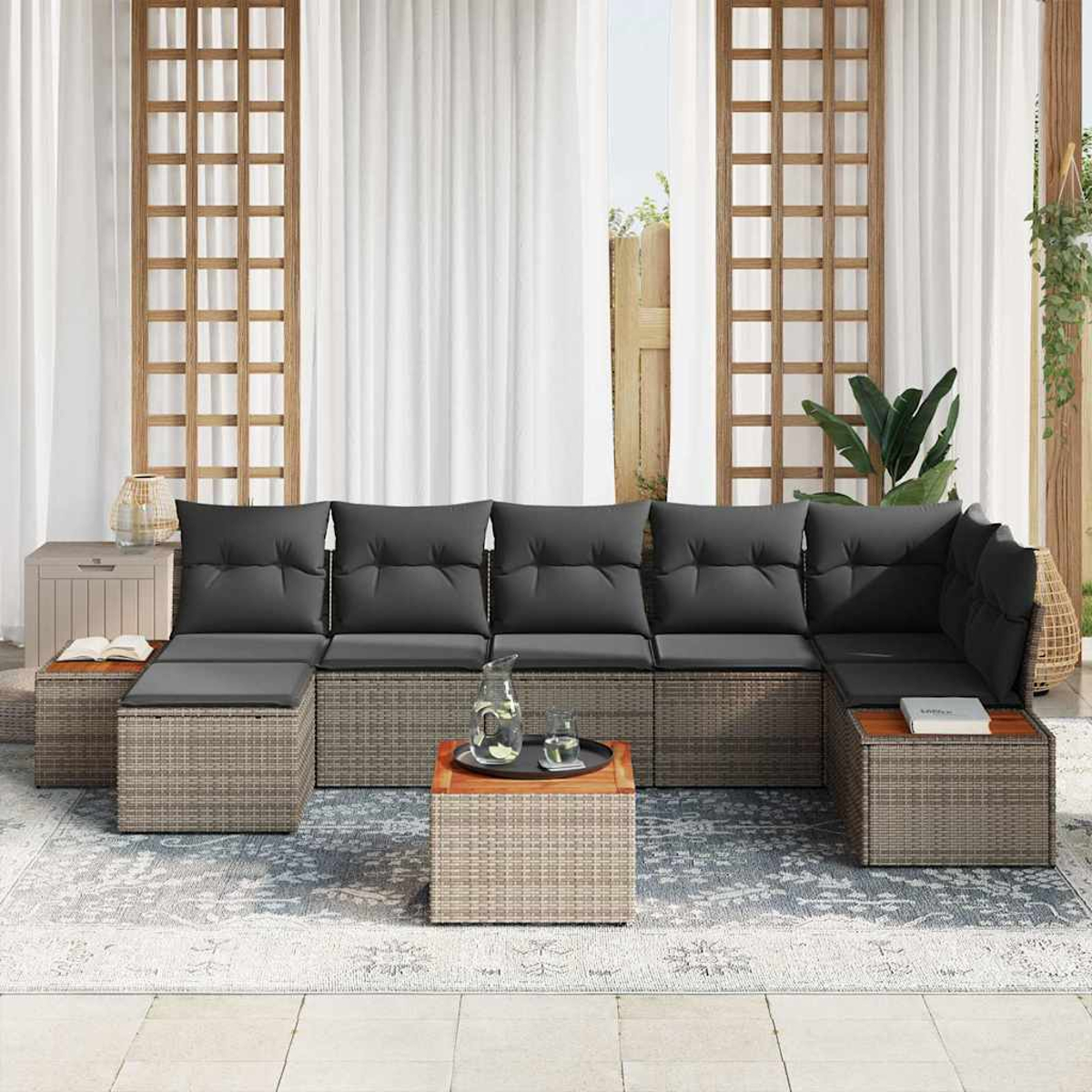 Outdoor-Ecksofa mit grauen Kissen, zwei Holztischen und einem Rattantisch, auf einem gemusterten Teppich. Weiße Vorhänge im Hintergrund.