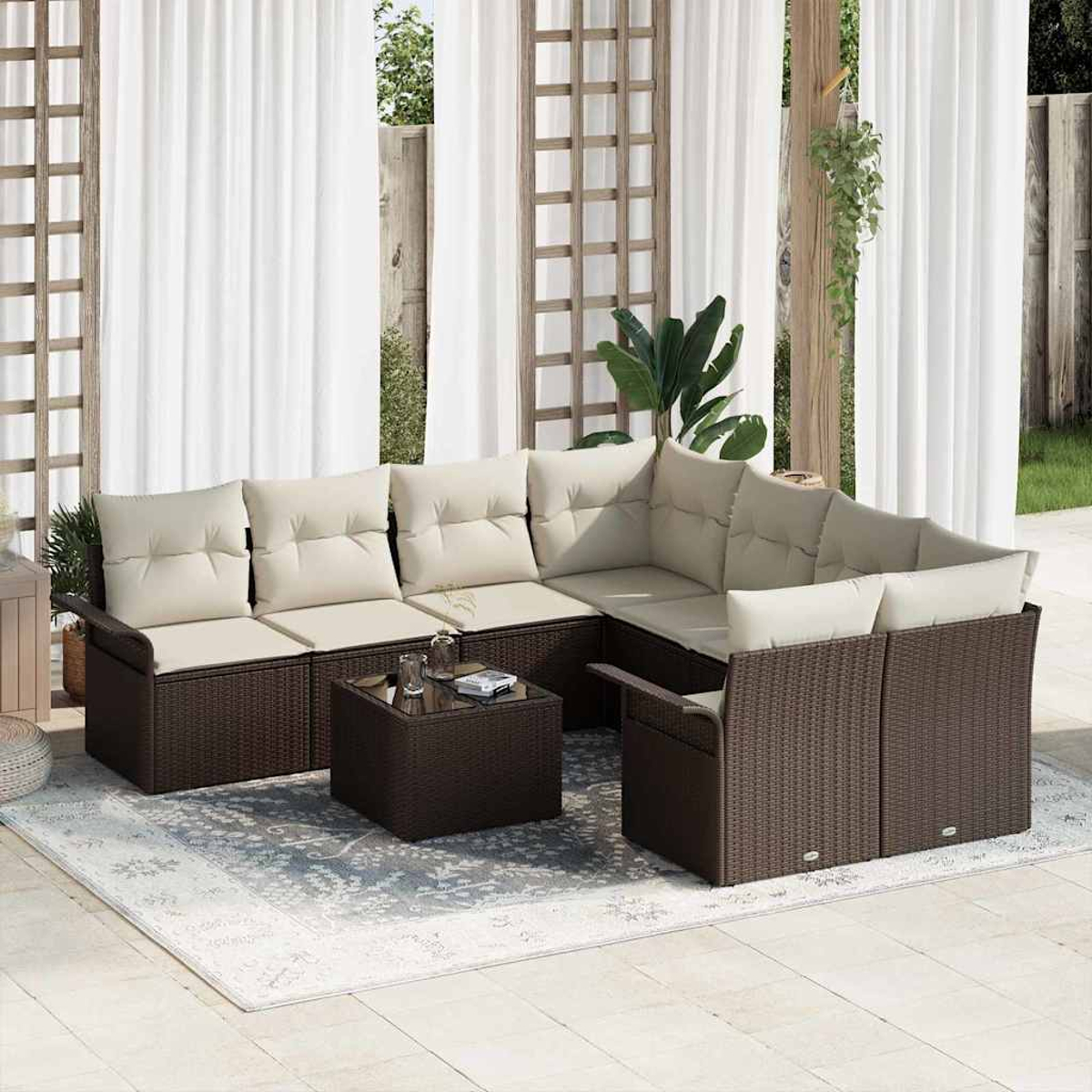 Juego de muebles de patio exterior con marcos de mimbre marrón y cojines beige. Incluye una mesa de centro sobre una alfombra estampada, cortinas al fondo.