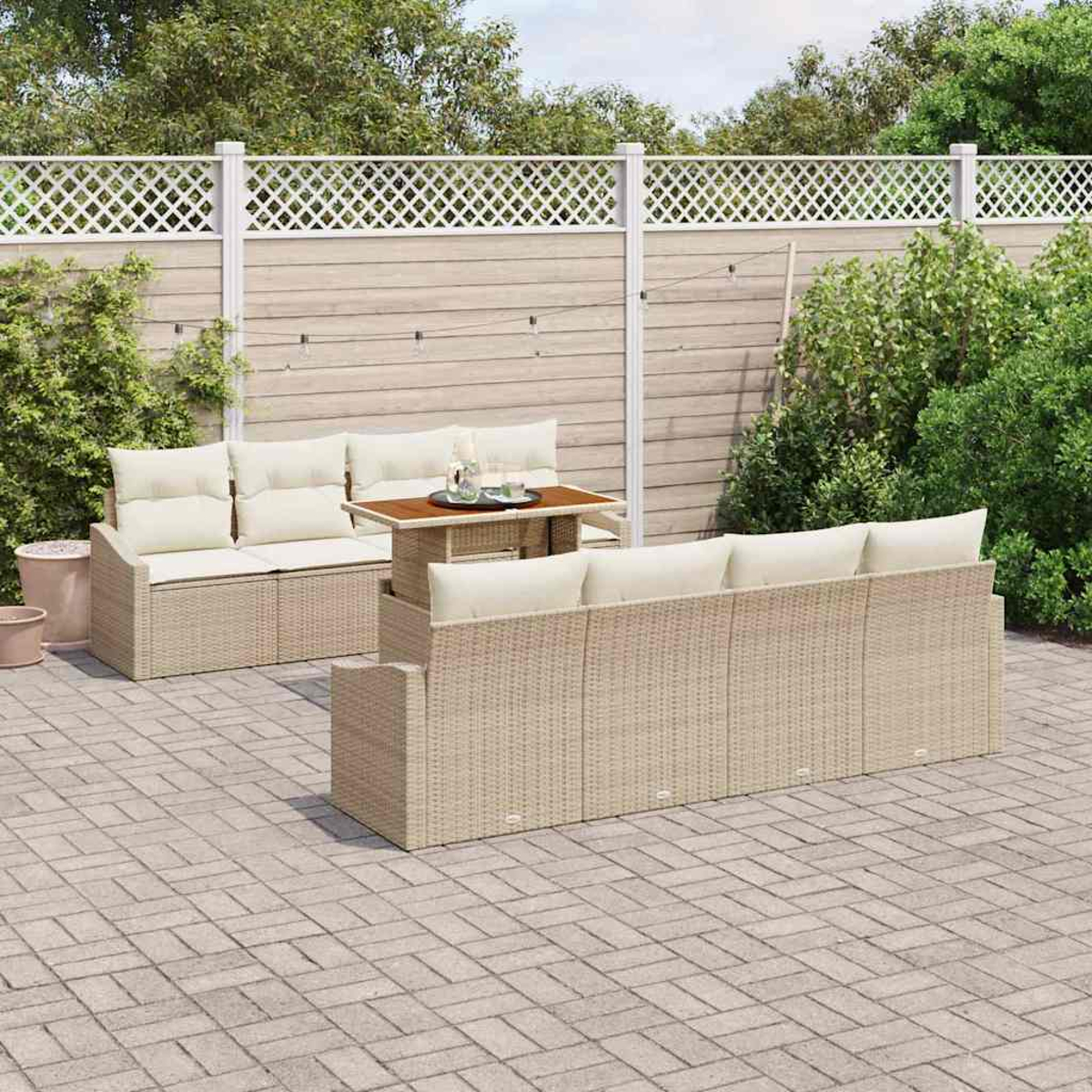 Terrasse mit beigen Rattansofas, Kissen und einem kleinen Tisch. Ein weißer Zaun und Grünzeug im Hintergrund.