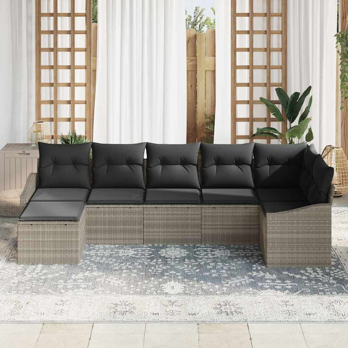 Outdoor-Ecksofa mit schwarzen Kissen, auf einem gemusterten Teppich, vor weißen Vorhängen und Holzgitter.