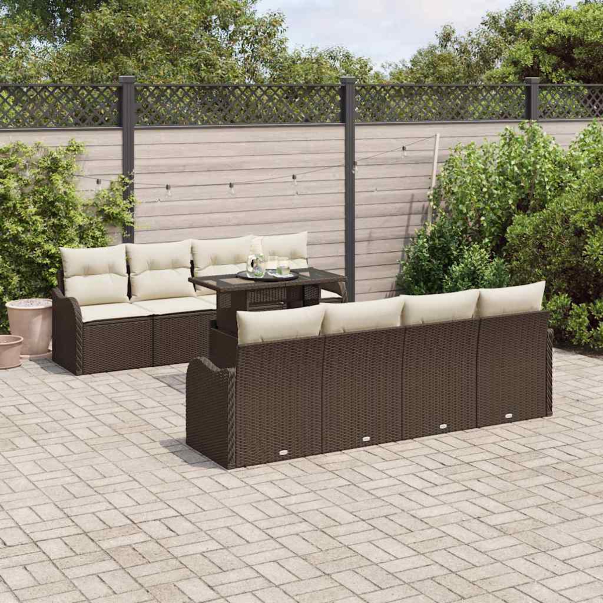 Terrassengarnitur: braune Korbsessel mit cremefarbenen Kissen, kleiner Tisch und gepflasterte Terrasse, umgeben von Pflanzen und einem Zaun.