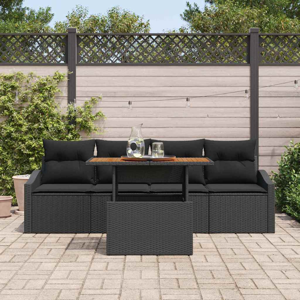 Terrassengarnitur: schwarzes Sofa mit Kissen, Tisch mit Getränken und Zaun im Hintergrund. Ziegelboden.