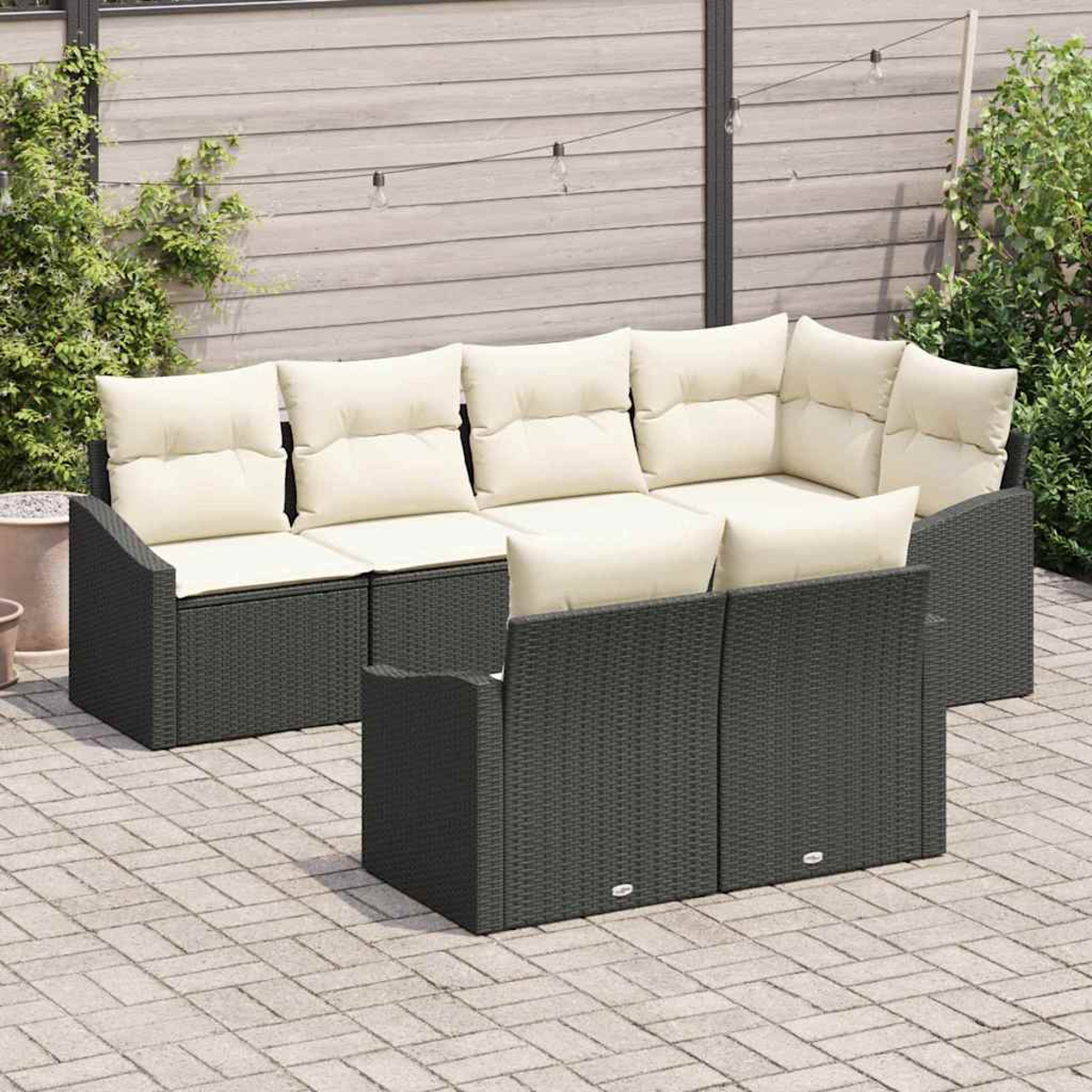 Gartensektionssofa mit cremefarbenen Kissen, dunkelgrauem Korbgeflecht und Ziegelpflaster. Hintergrund mit Pflanzen und Lichterketten.