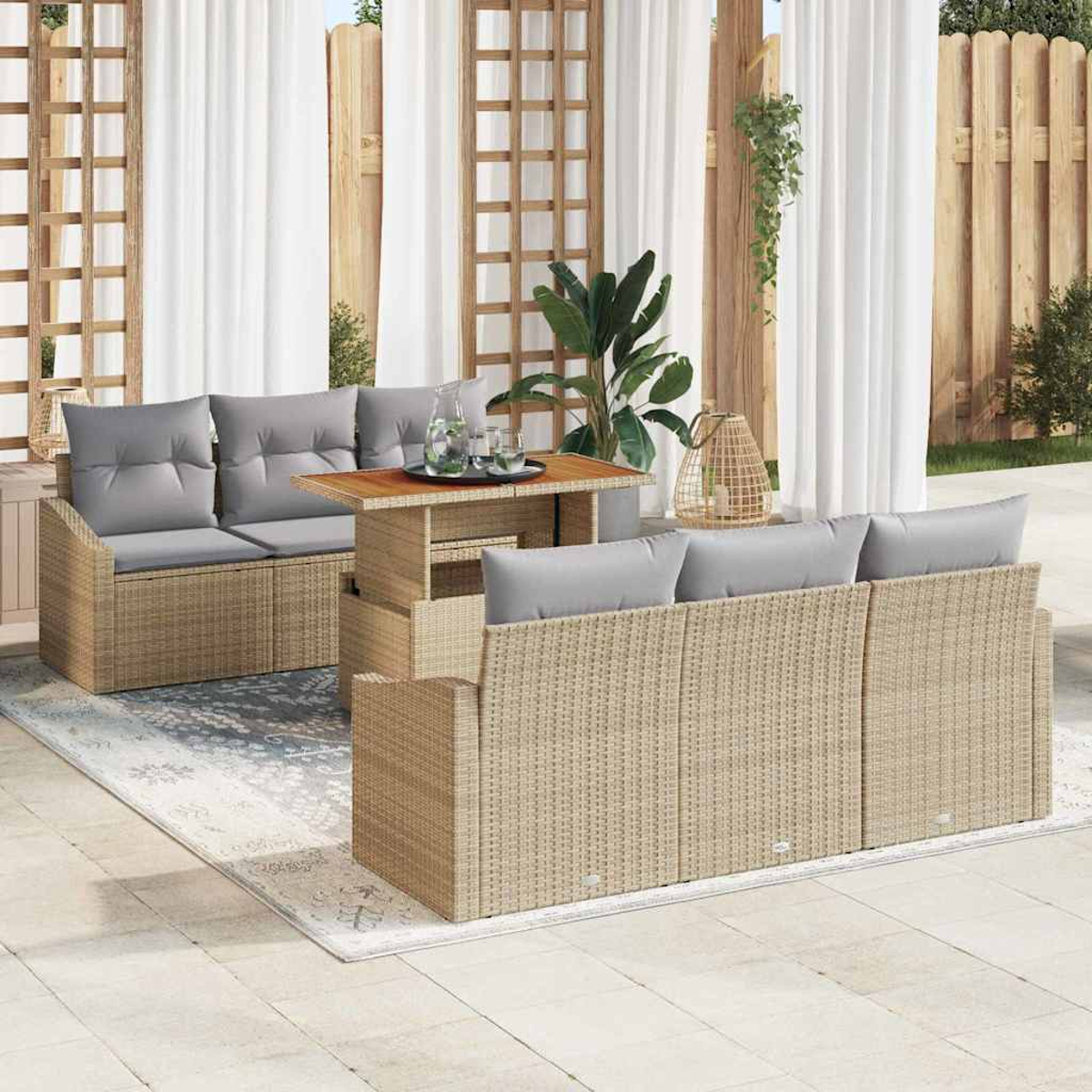 Gartenmöbel-Set aus Rattan mit grauen Kissen, Holztisch und weißen Vorhängen im Hintergrund.