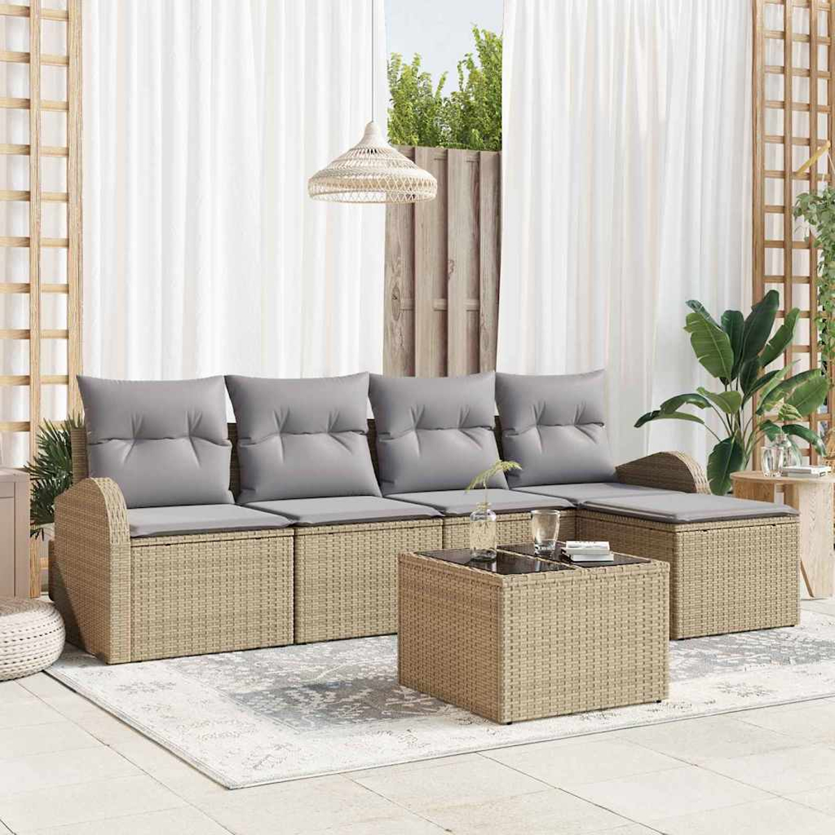Ein beiges Rattansofa mit grauen Kissen, ein passender Couchtisch und ein Teppich stehen auf einer Terrasse. Vorhänge und Pflanzen sind im Hintergrund.