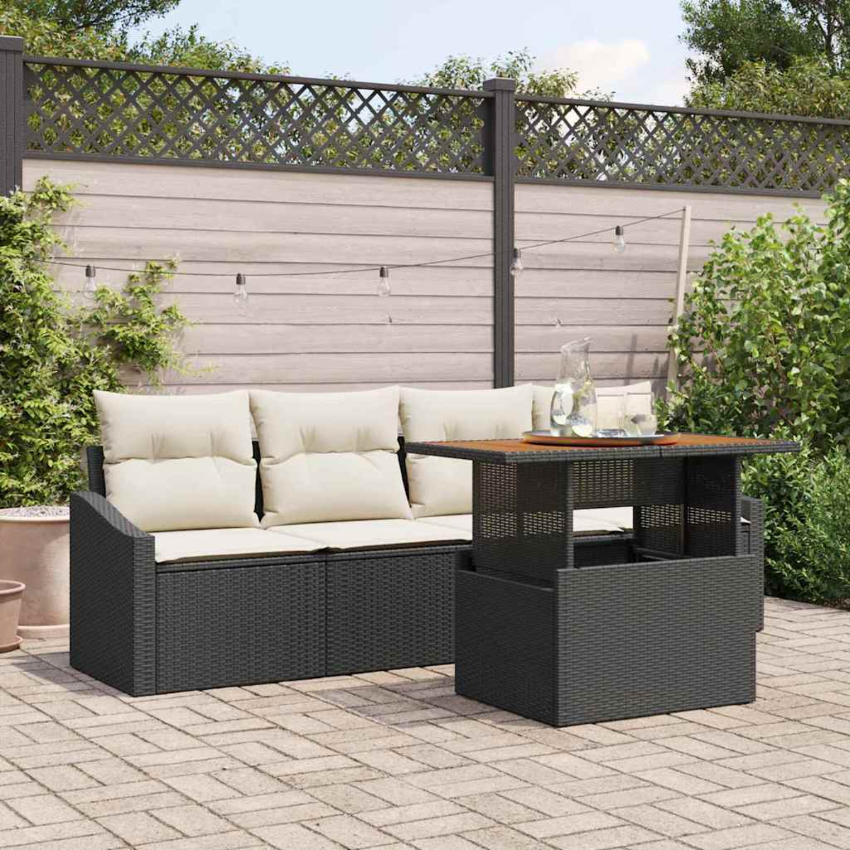 Szene im Freien mit dunklem Rattansofa und -tisch. Creme-Kissen auf dem Sofa. Tischplatte aus Holz. Ziegelpflaster mit Holzzaun.