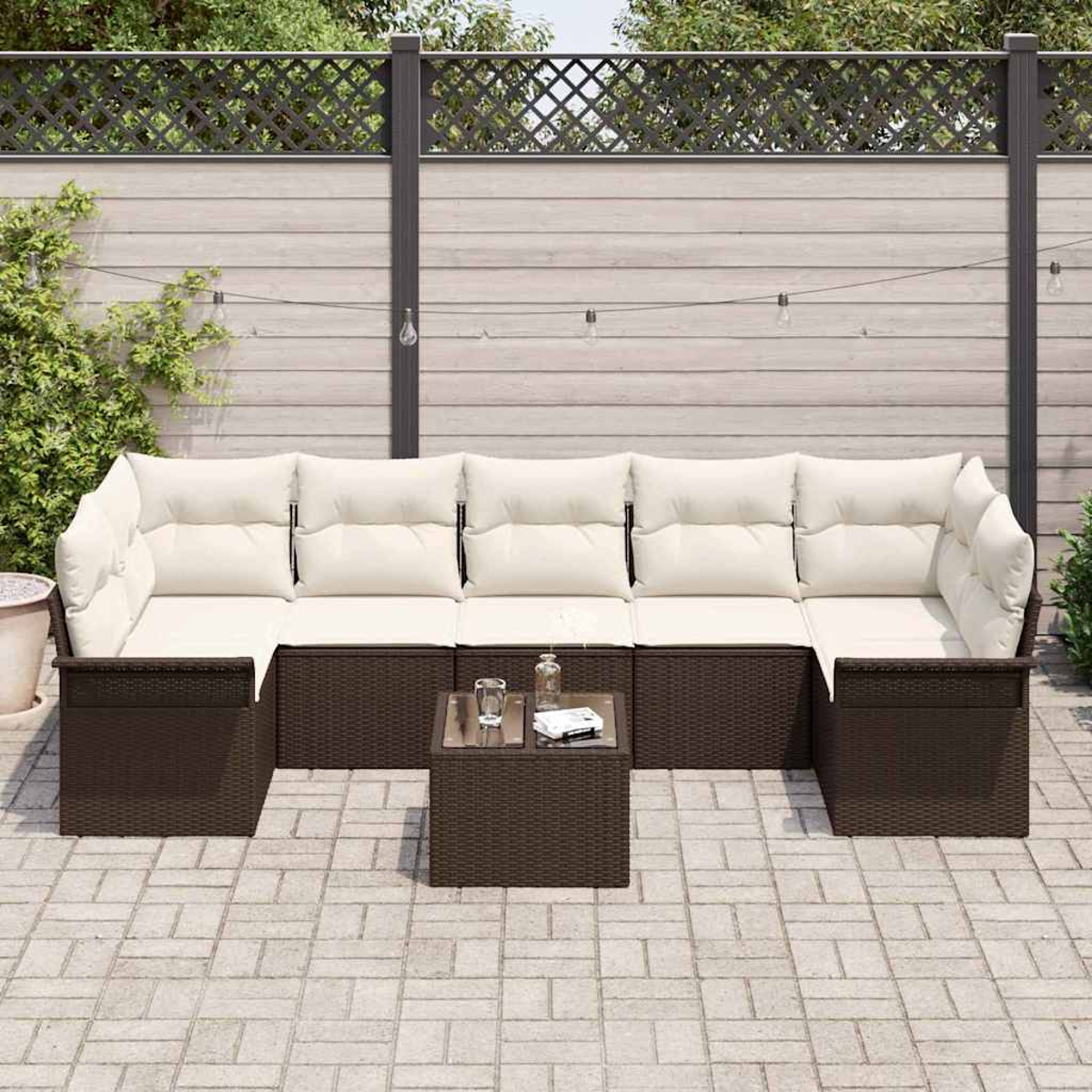 Garten-Set mit braunem Korbgewebe und cremefarbenen Kissen. Ein kleiner Tisch und eine Ziegelterrasse mit Holzzaun im Hintergrund.