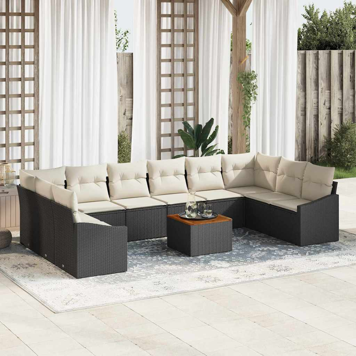 Outdoor-Sitzgruppe mit cremefarbenen Kissen. Ein quadratischer Tisch mit Gläsern steht auf einem gemusterten Teppich. Weiße Vorhänge sind im Hintergrund.
