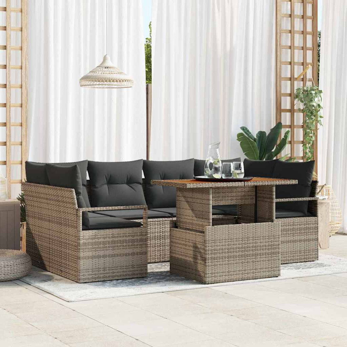 Terrassenset mit Tisch und Sofa. Enthält dunkelgraue Kissen, hellbraunes Korbgeflecht und weiße Vorhänge im Hintergrund.