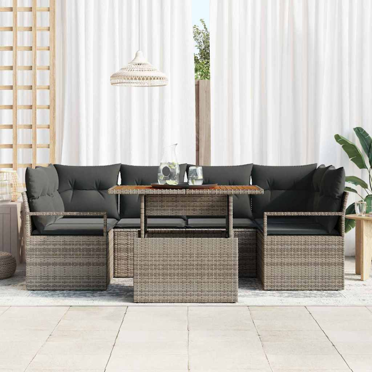 Gartenmöbel-Set mit grauen Kissen, Rattangestellen und einem Holztisch. Weiße Vorhänge im Hintergrund und eine Hängelampe.