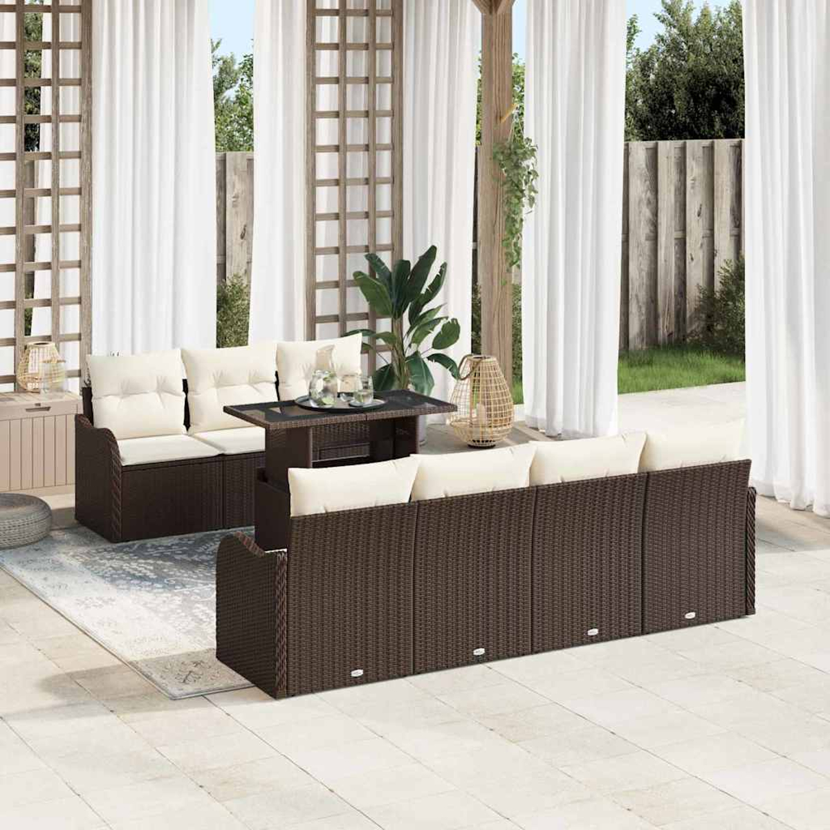 Garten-Terrassenset mit braunen Korbsesseln, cremefarbenen Kissen und einem dunklen Tisch. Weiße Vorhänge und ein Holzzaun sind im Hintergrund.