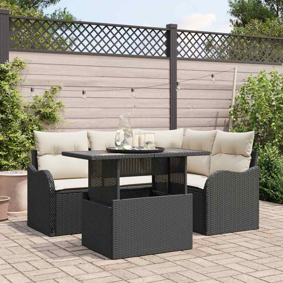 Garten-Terrassenset mit schwarzen Korbmöbeln, beigen Kissen und einem Hubtisch. Hintergrund: Zaun, Pflanzen und eine Backsteinterrasse.