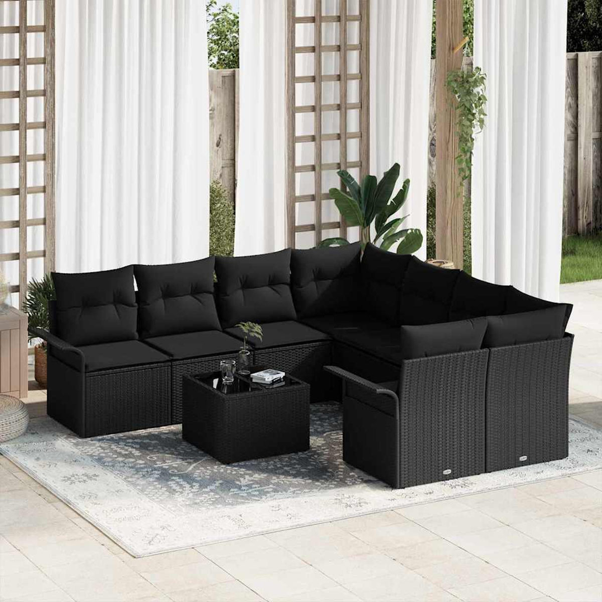 Outdoor-Ecksofa mit schwarzen Kissen und Couchtisch. Vorhänge und Pflanzen im Hintergrund, alles auf einer Terrasse.