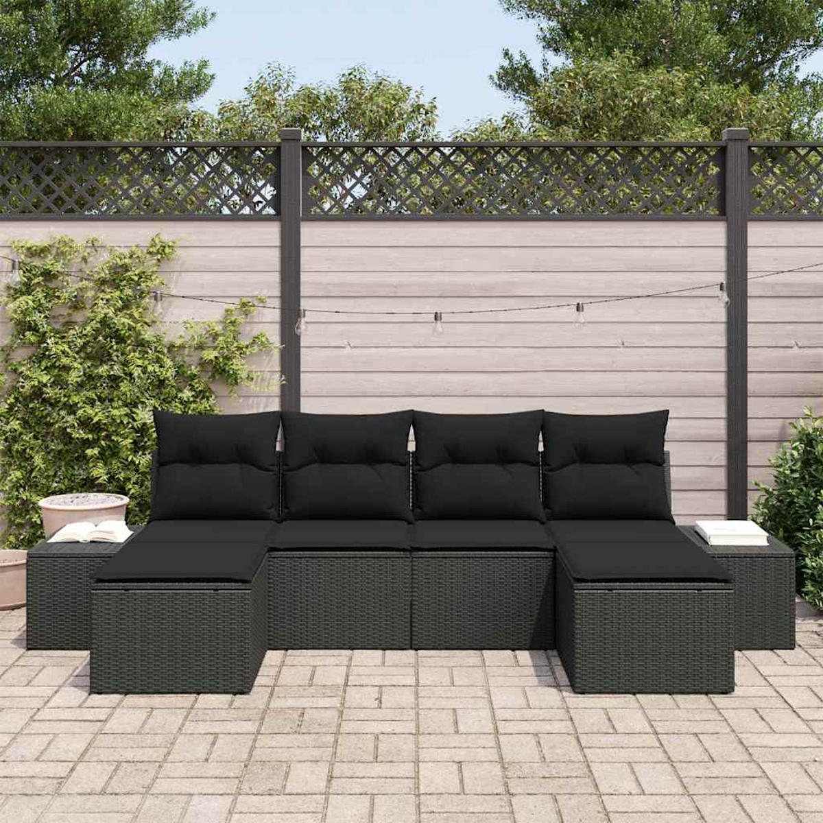 Schwarzes Outdoor-Wicker-Sofa mit schwarzen Kissen auf einer Terrasse. Im Hintergrund Holzlattenzaun und Grün.