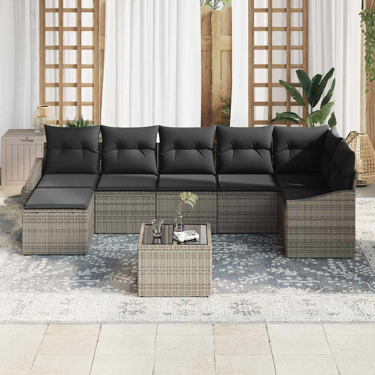 Un sofá seccional al aire libre con cojines negros y una mesa pequeña. El sofá está sobre una alfombra estampada, con un enrejado de madera al fondo.