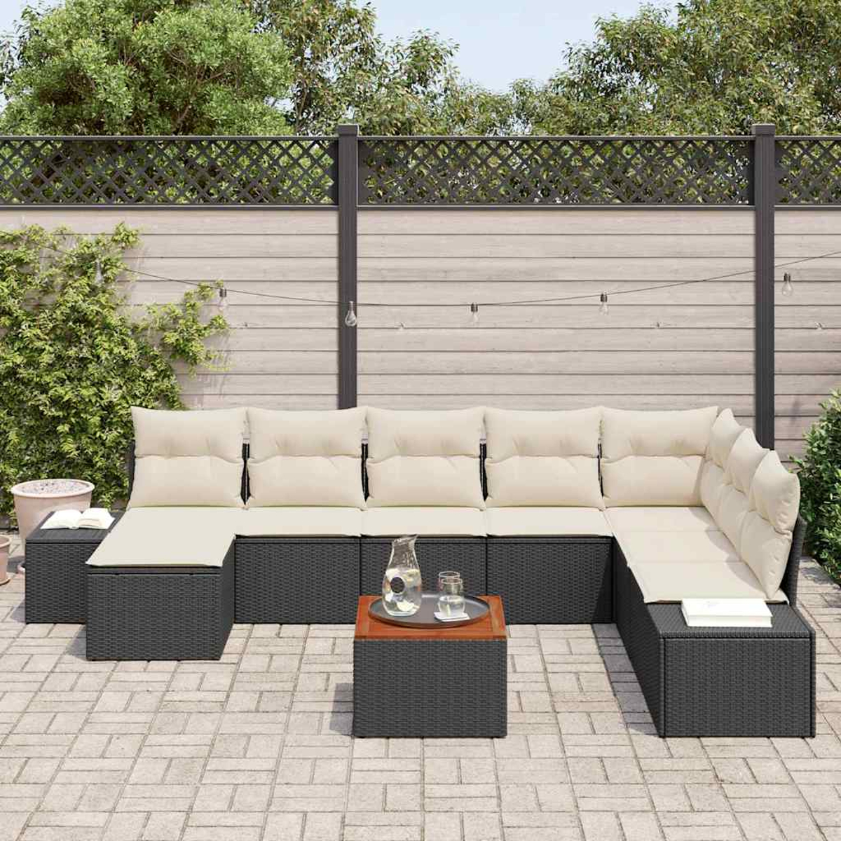 Outdoor-Ecksofa mit beigen Kissen und einem kleinen Tisch. Auf dem Tisch stehen eine Wasserkaraffe und Gläser, der Hintergrund ist ein Zaun.