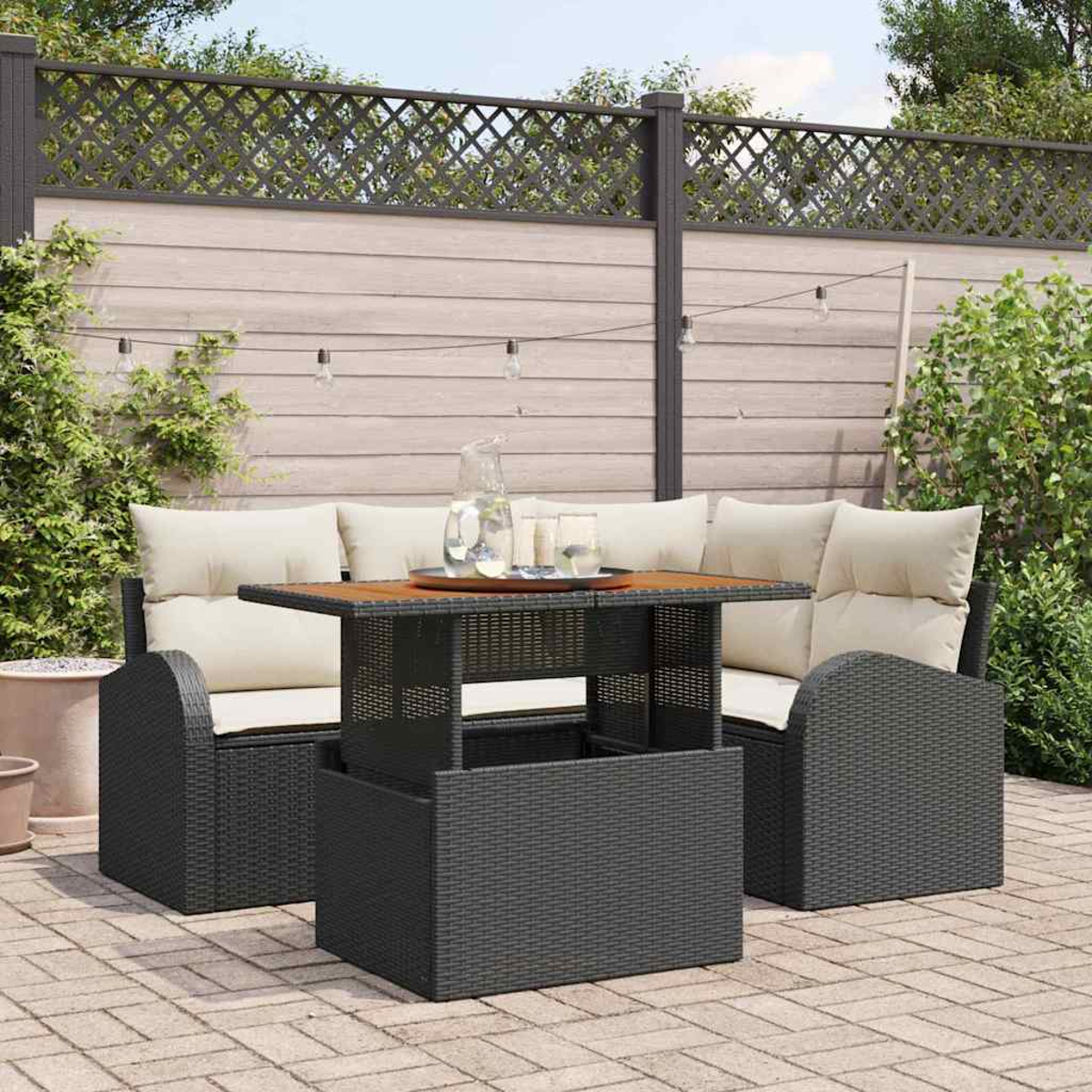 Gartenmöbel-Set. Dunkelgraue Sitzgelegenheiten mit cremefarbenen Kissen, Holztisch, Gläsern und einem Krug. Hinterhof-Umgebung.