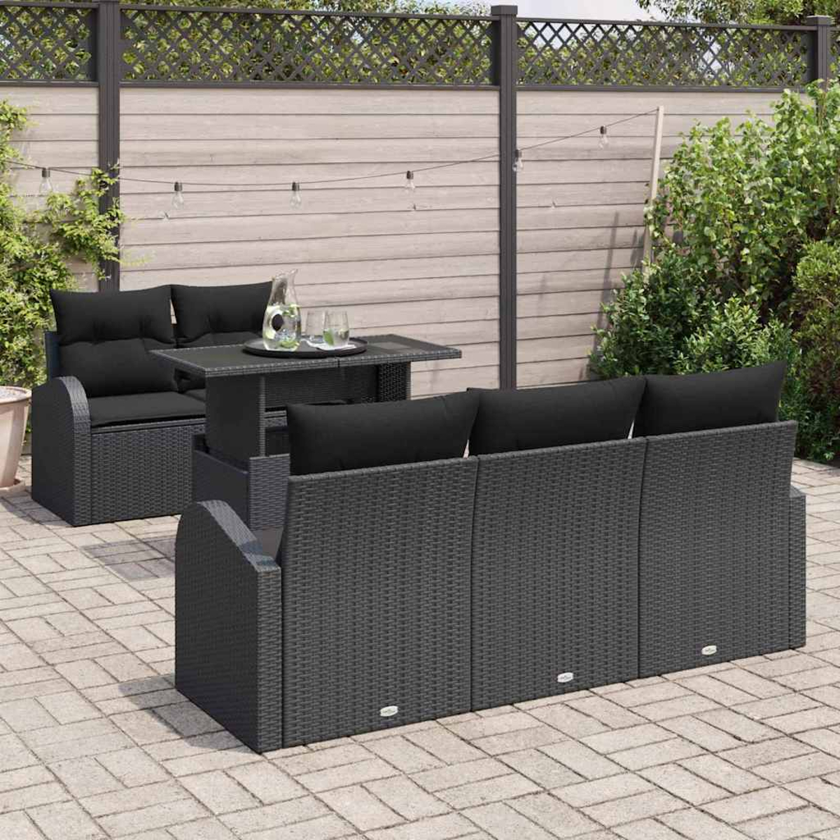Ein schwarzes Outdoor-Möbelset aus Korbgeflecht auf einer Terrasse. Es umfasst ein Sofa, einen Tisch mit Getränken und einen Einzelsitz. Der Hintergrund ist ein Zaun.