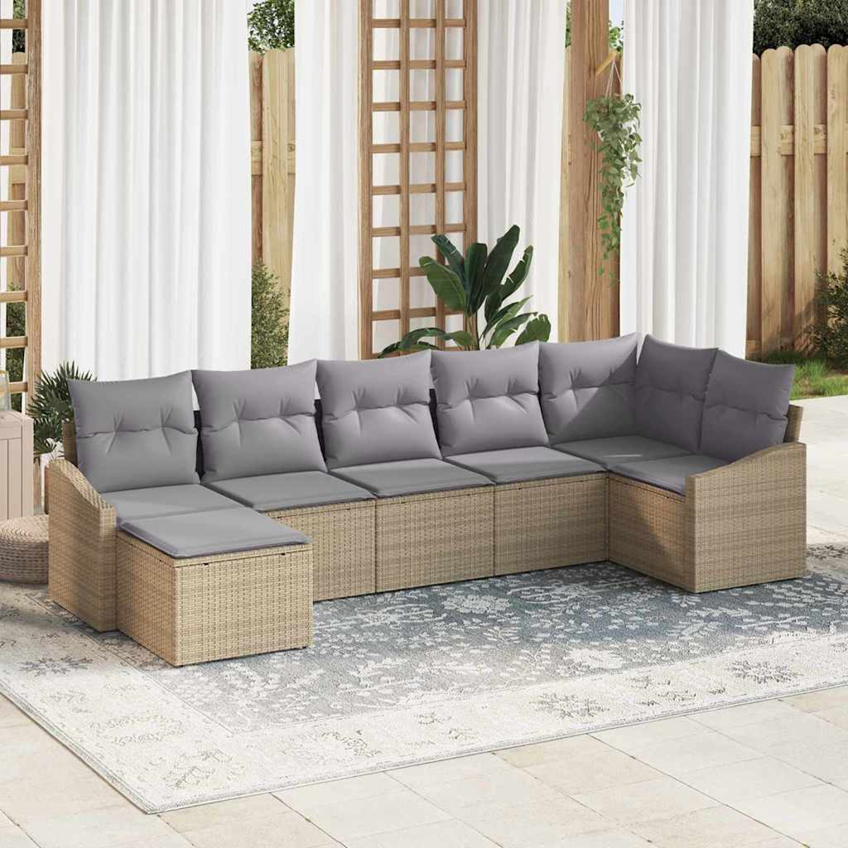 Ein beiges Rattan-Ecksofa mit grauen Kissen steht auf einem gemusterten Teppich. Im Hintergrund befinden sich weiße Vorhänge und Holzkonstruktionen.