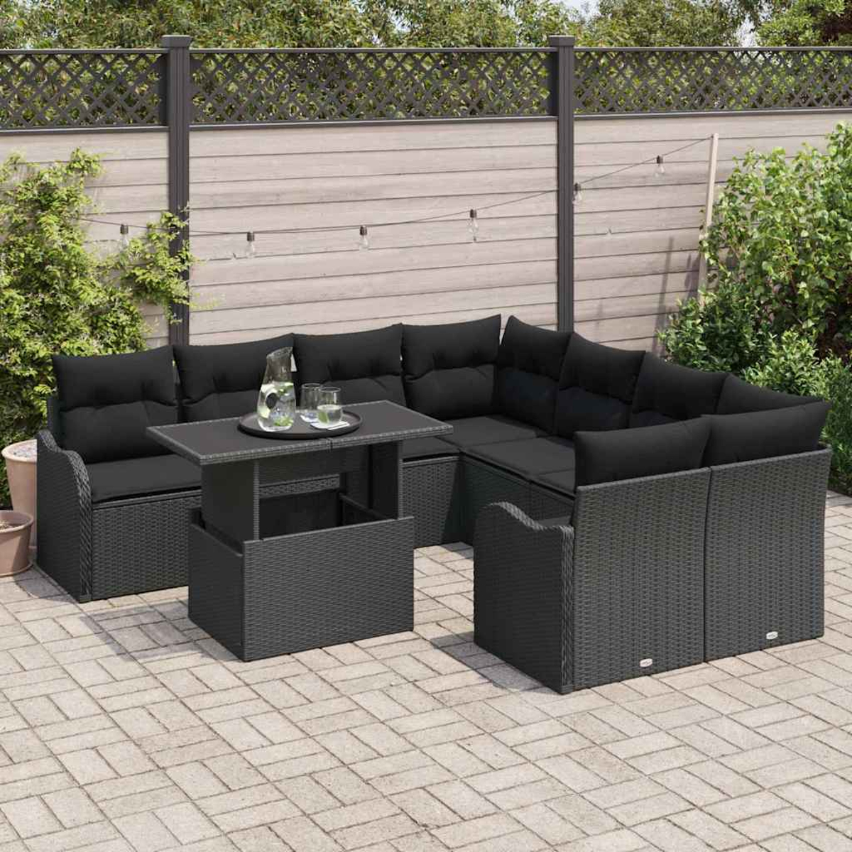 Juego de patio al aire libre con cojines negros, una mesa con bebidas y una valla de madera al fondo.