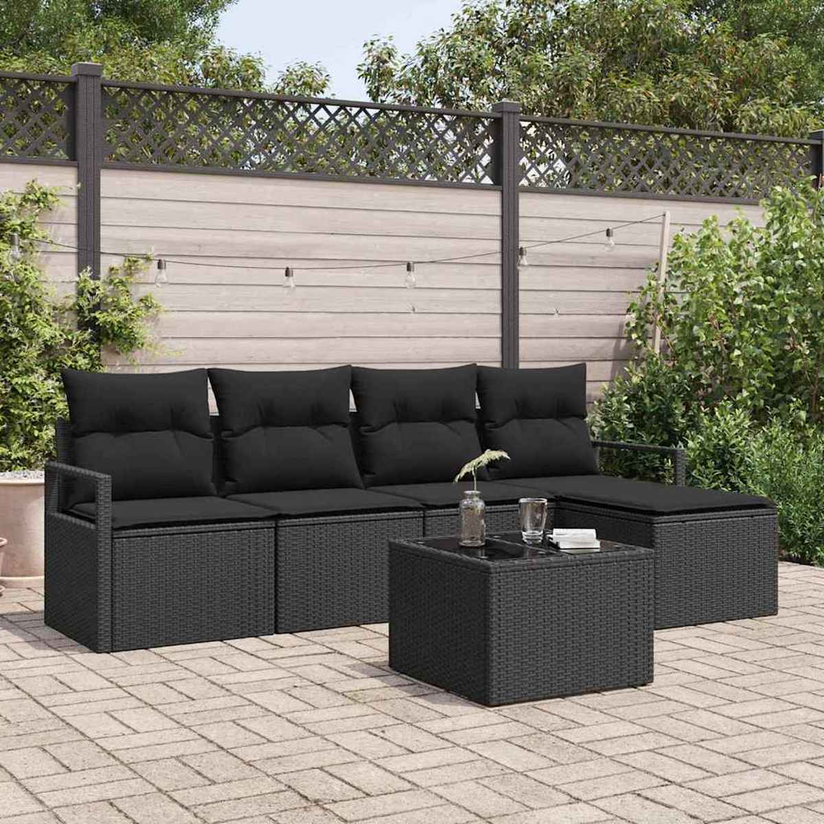 Terrassenset mit schwarzen Kissen. Enthält Sofa, Ottomane und Couchtisch, alles auf einer Ziegelterrasse mit Holzzaun.