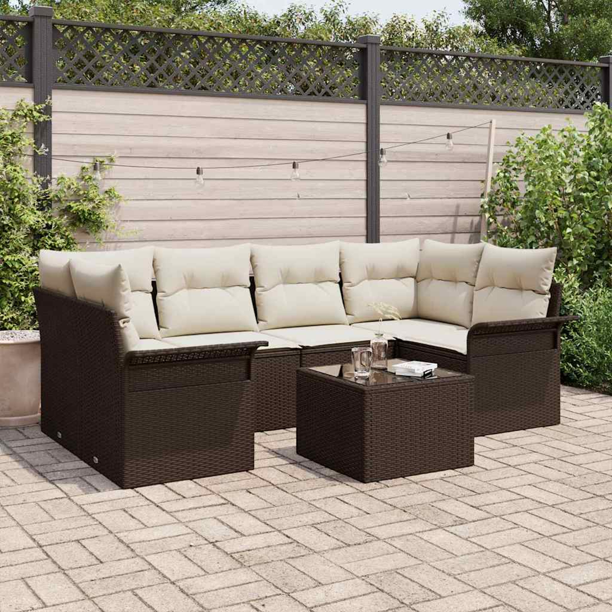 Garten-Set mit braunem Korbmöbel-Sofa und Tisch, cremefarbenen Kissen, auf einer Backstein-Terrasse. Zaun und Grün im Hintergrund.