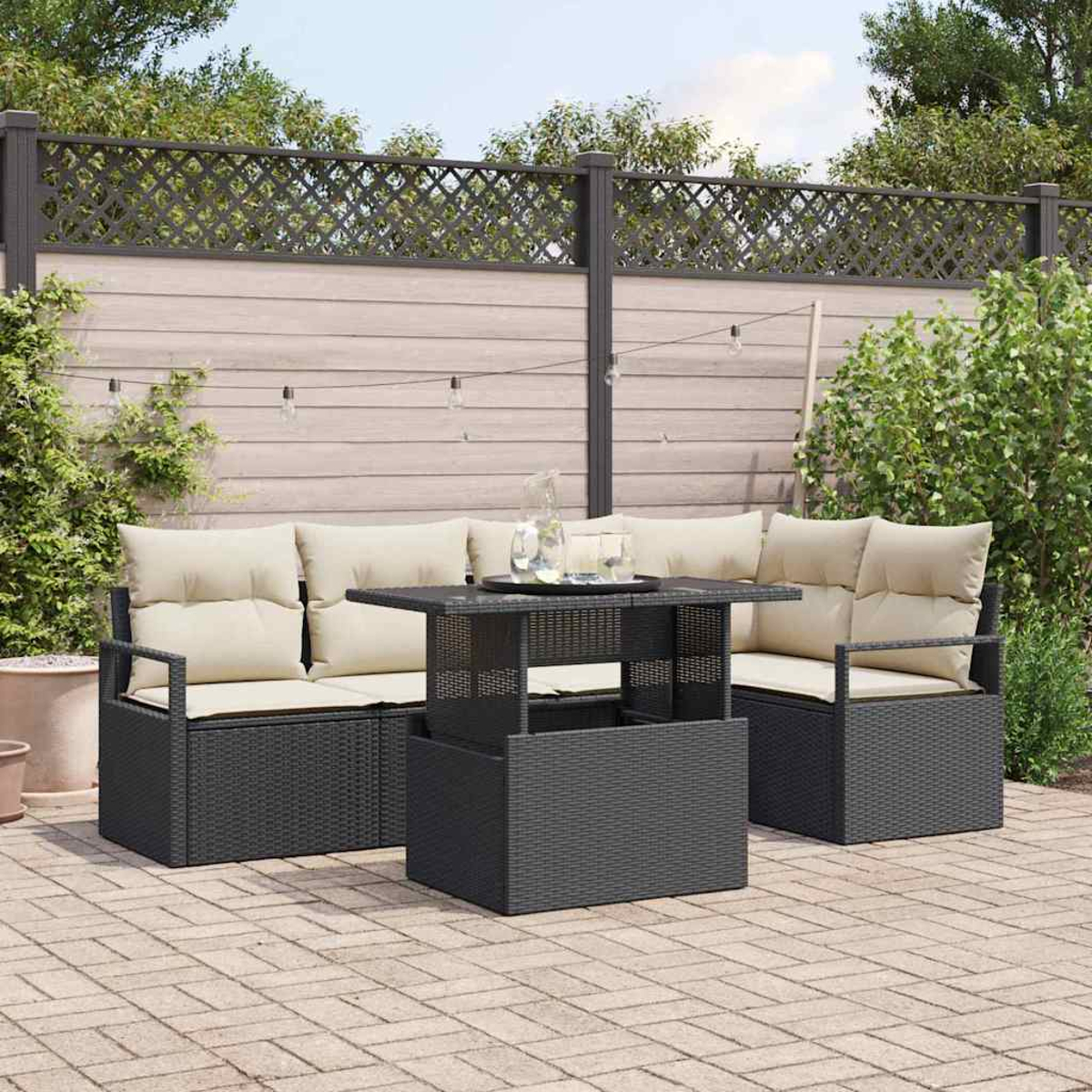 Terrassenset mit schwarzen Möbeln, cremefarbenen Kissen und einem Tisch mit Hubfunktion. Hintergrund: Zaun und Grün.