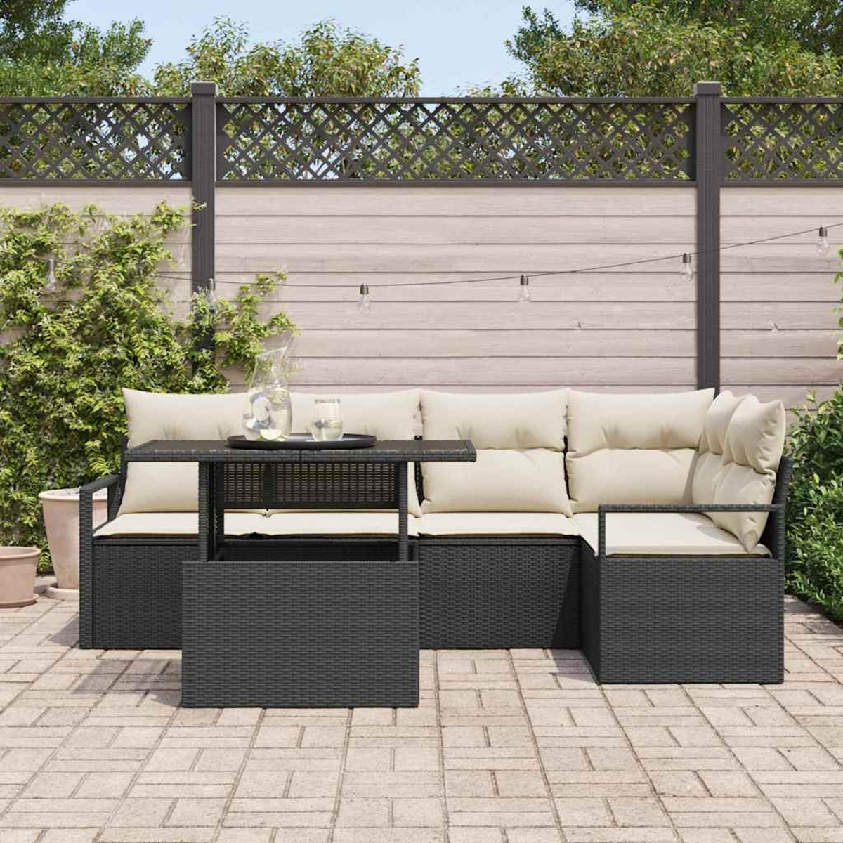 Gartenmöbel-Set aus Korbgeflecht mit beigen Kissen. Ein Tisch mit Getränken, ein Zaun und Grün im Hintergrund. Die Szene wirkt entspannt.