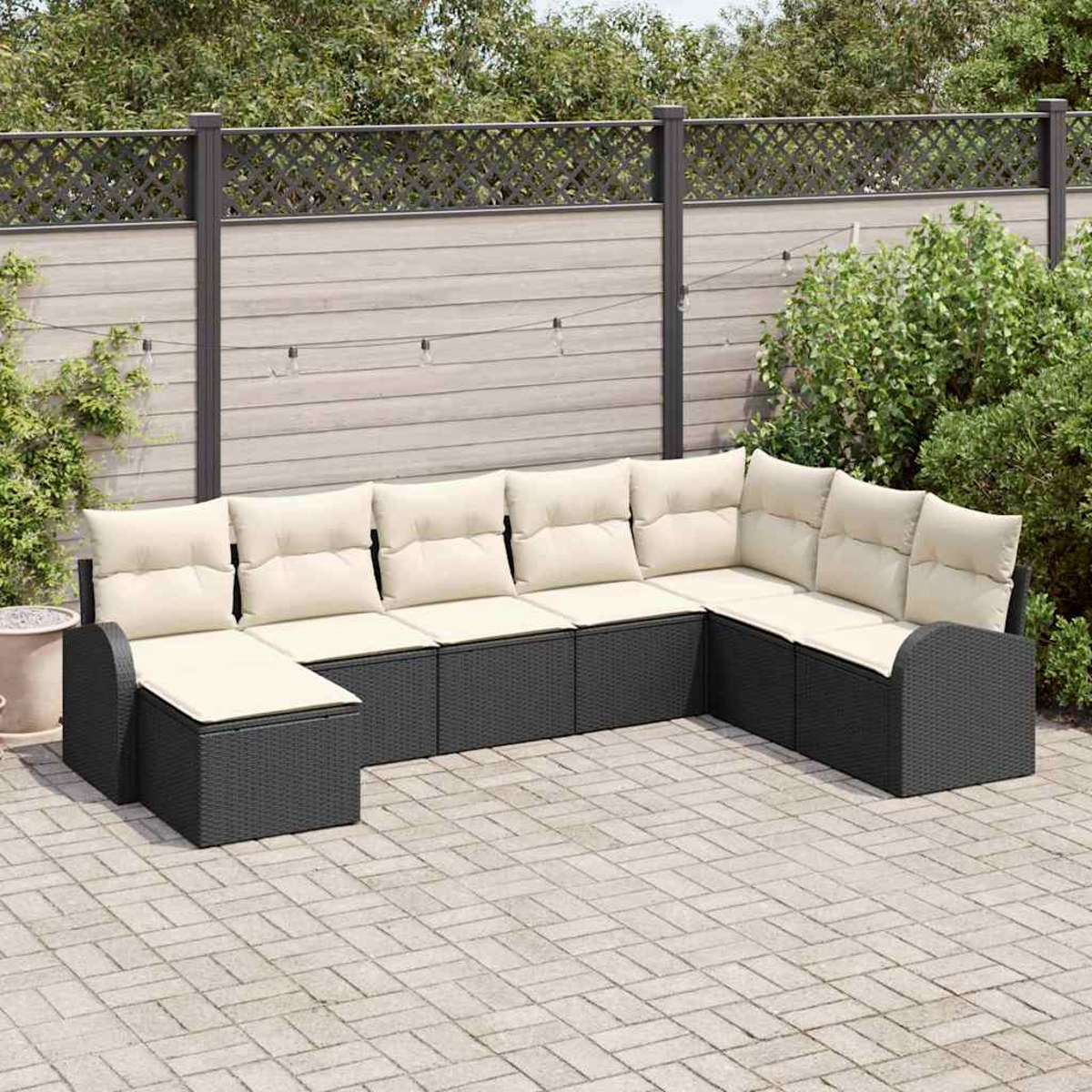 Ein Ecksofa im Freien mit cremefarbenen Kissen steht auf einer Ziegelterrasse. Im Hintergrund befinden sich ein Holzzaun und grüne Pflanzen.