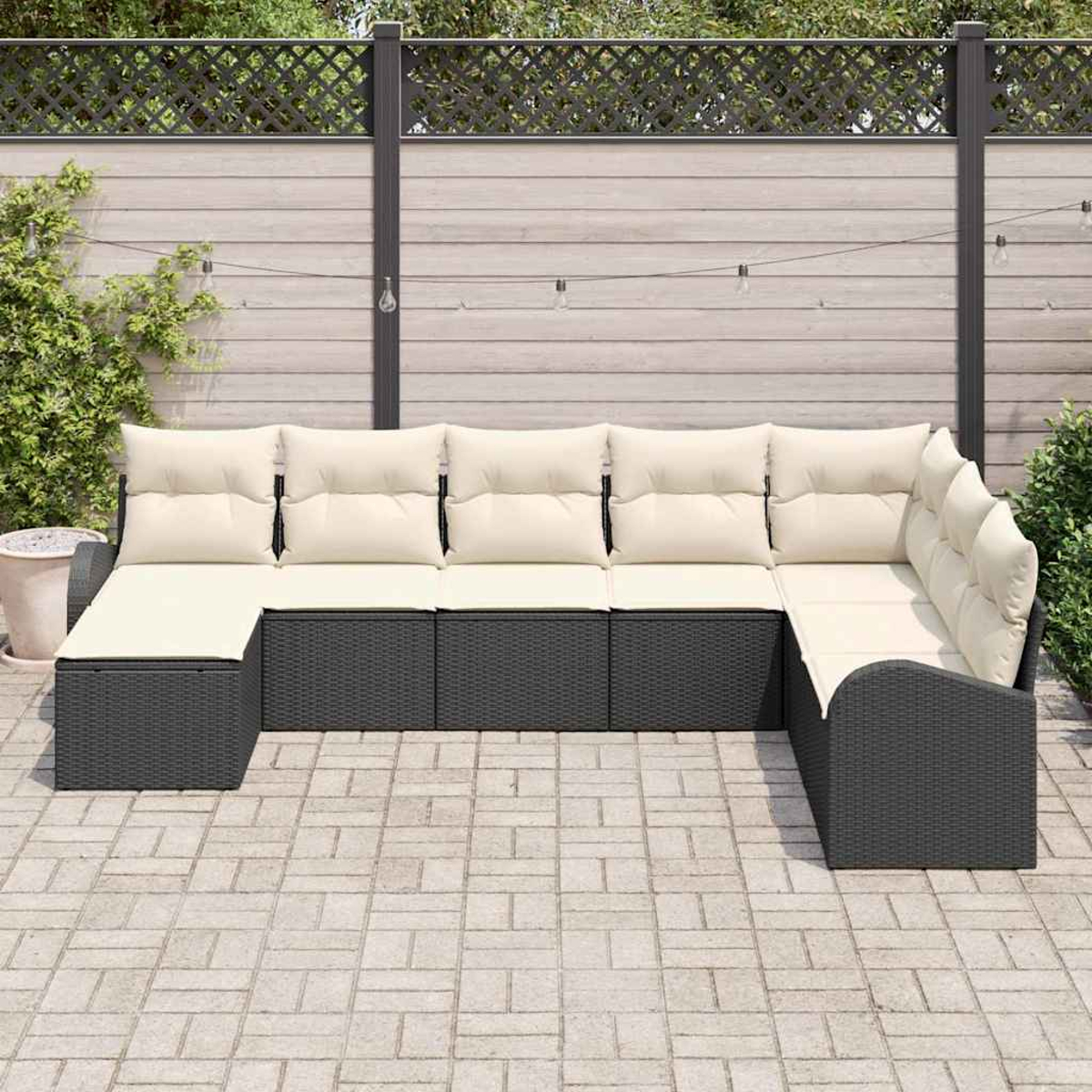 Ein Ecksofa im Freien mit cremefarbenen Kissen steht auf einer Backsteinterrasse. Im Hintergrund befinden sich ein Zaun und Pflanzen.