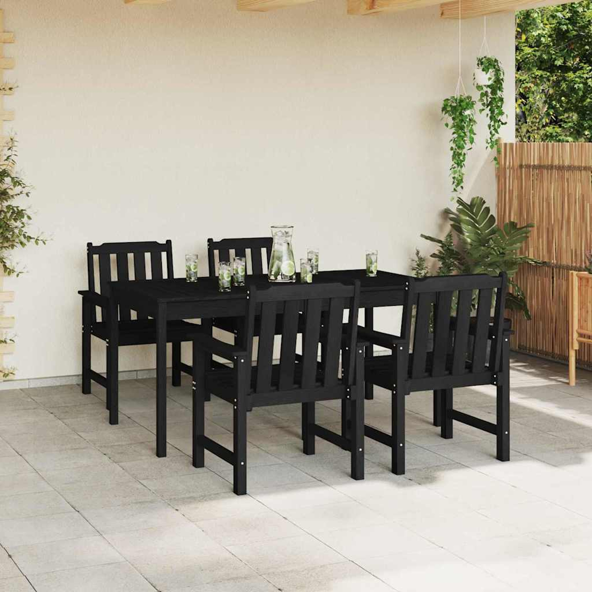 Juego de comedor al aire libre: mesa y sillas negras, bebidas en la mesa. Fondo: pared, plantas y valla de bambú. La escena es exterior.