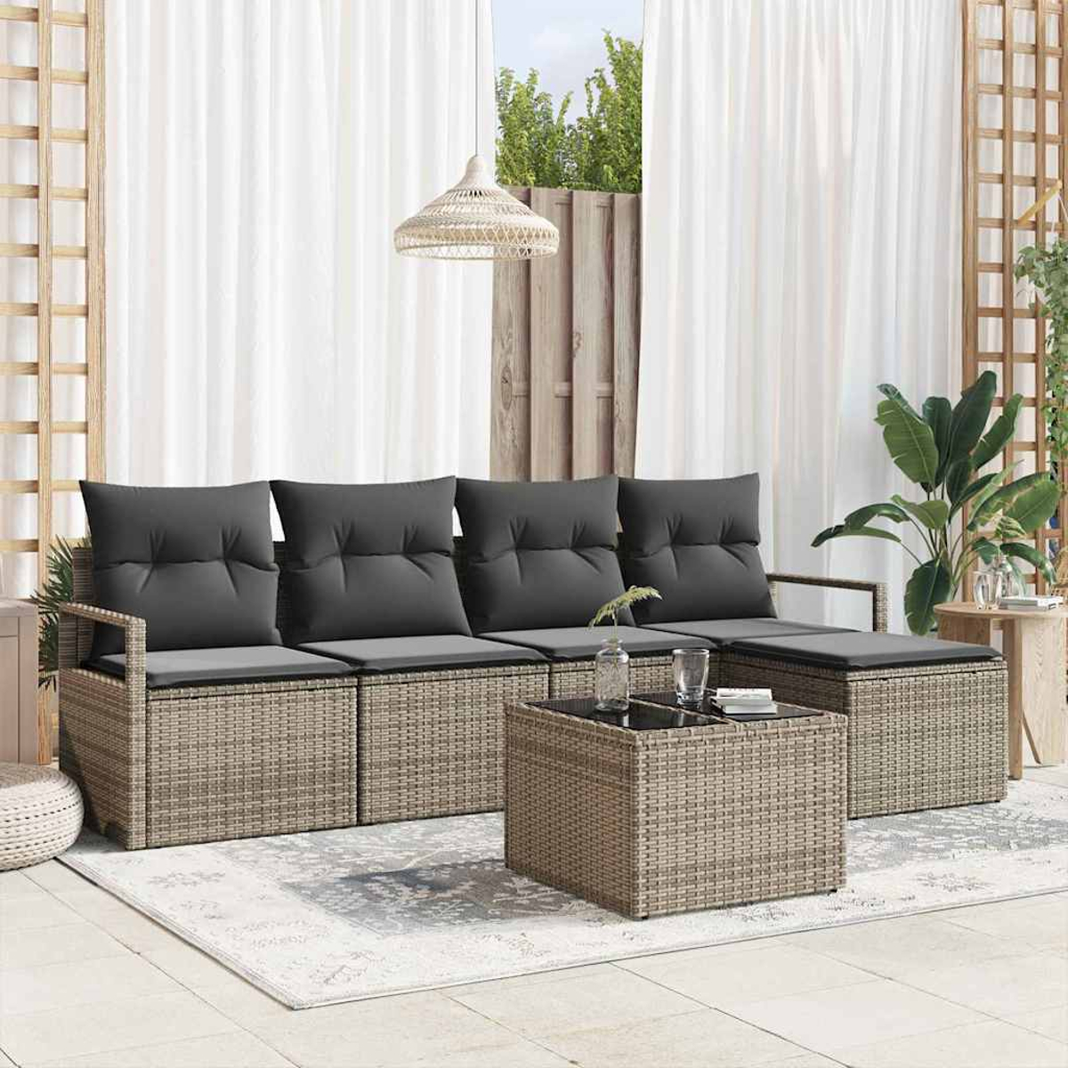 Outdoor-Sitzbereich mit grauen Kissen, Korbmöbeln, einem Teppich und einem Couchtisch. Weiße Vorhänge und Pflanzen im Hintergrund.